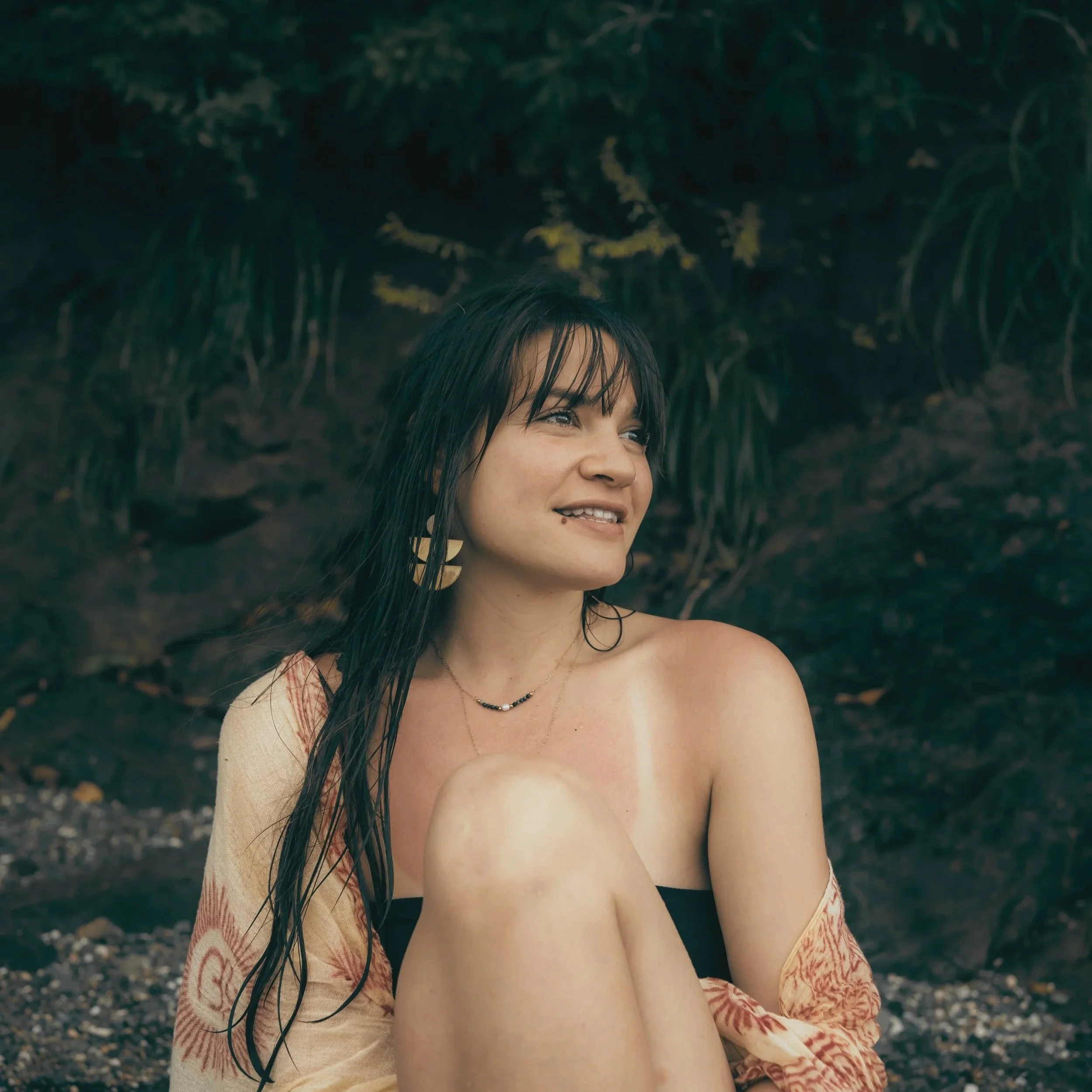 A woman with wet hair smiling outdoors near a lush green background.