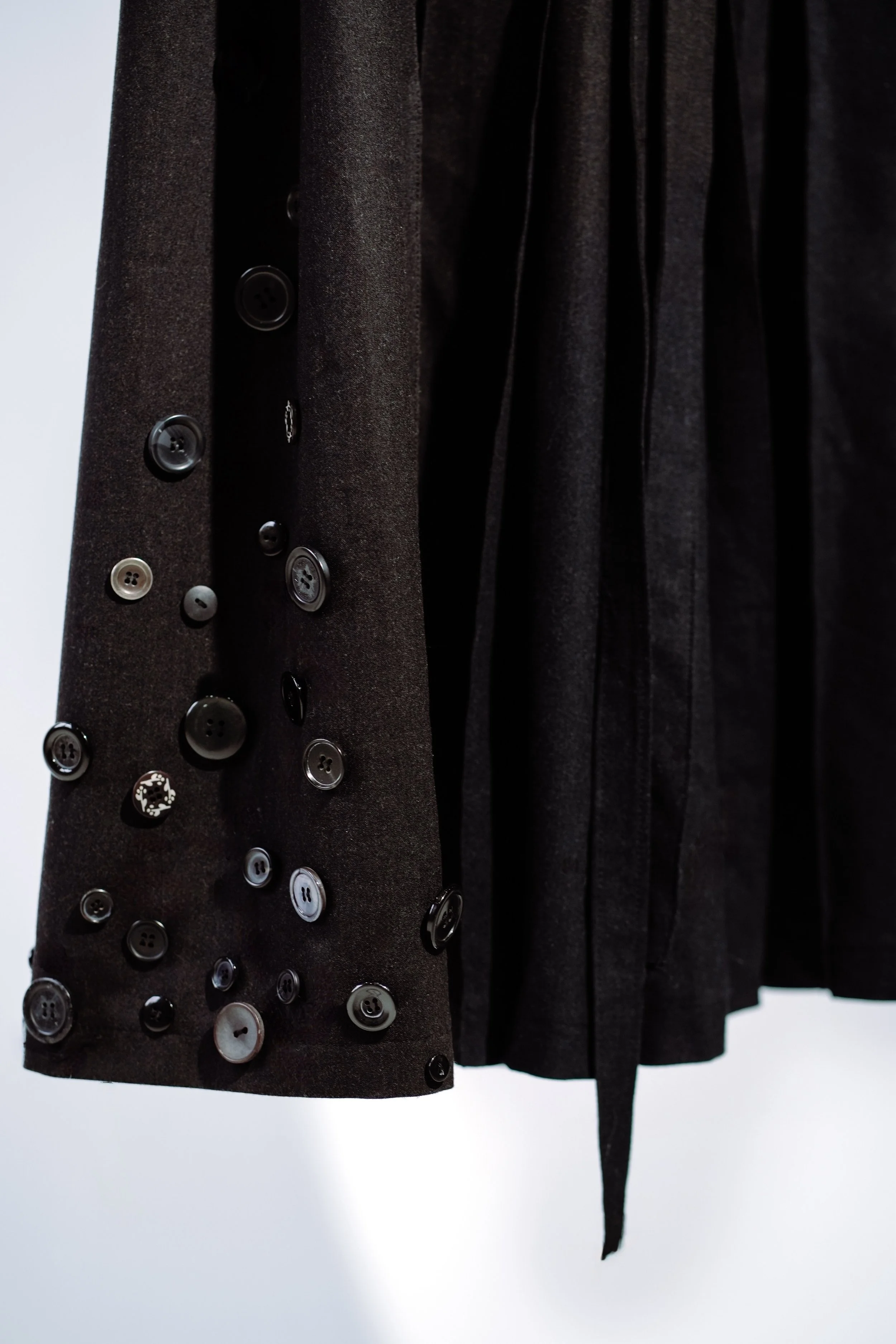 Close-up of a black garment with a sleeve decorated with various black, gray, and white buttons.