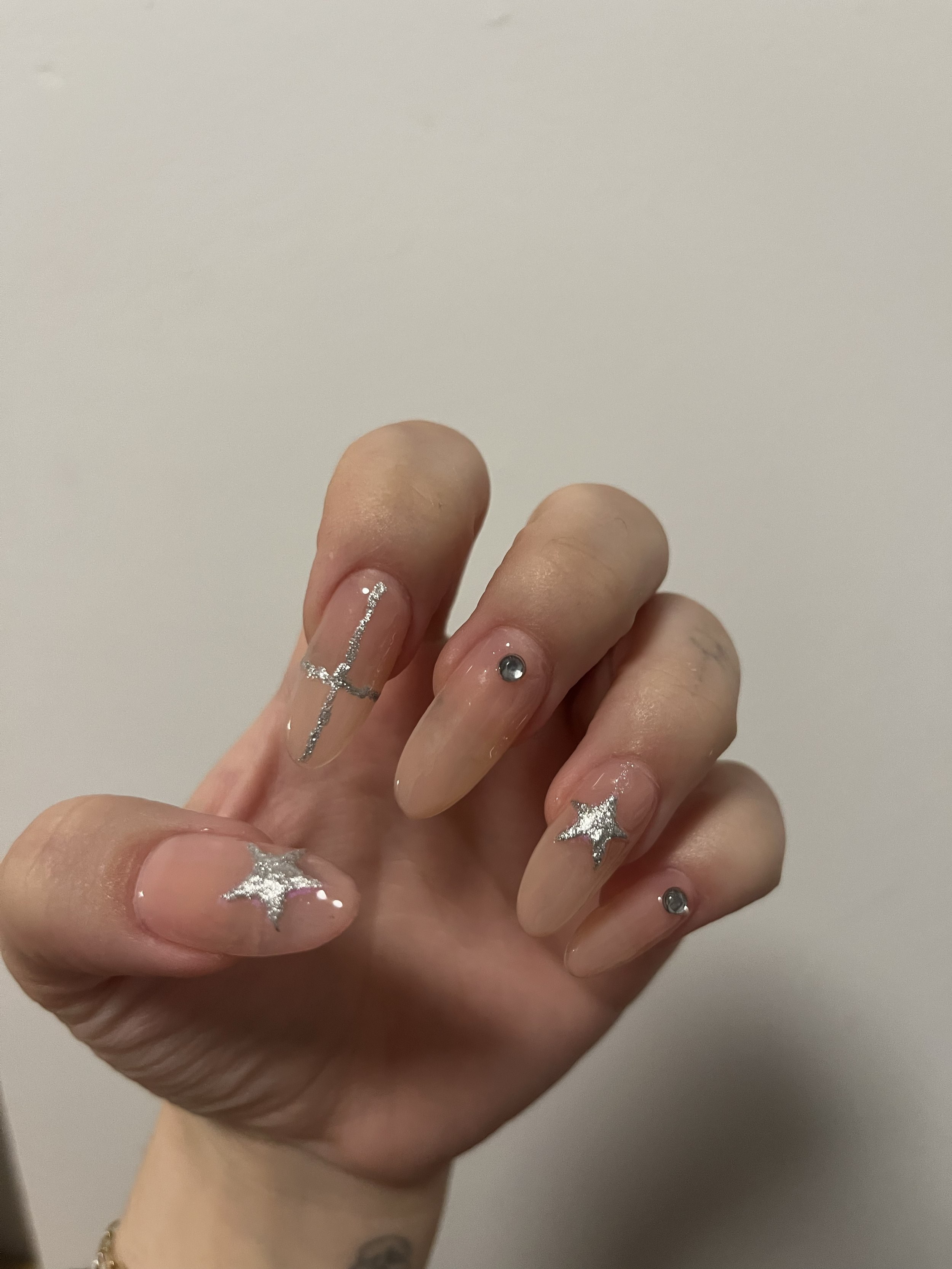 Hand with long, nude-colored nails decorated with silver glitter stars and rhinestones.