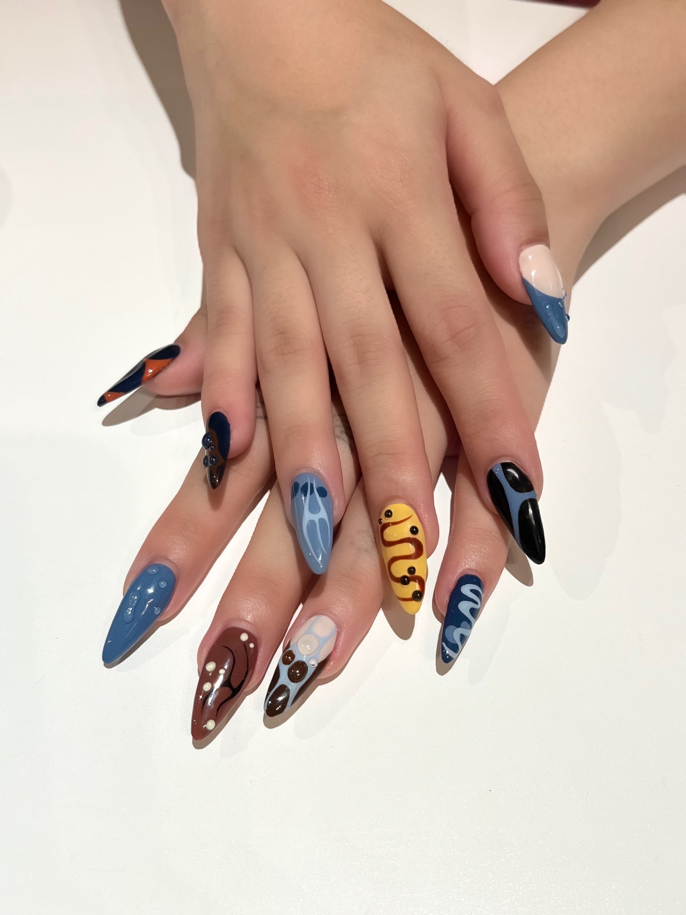 Nail art with various colorful designs on long, stiletto-shaped nails.