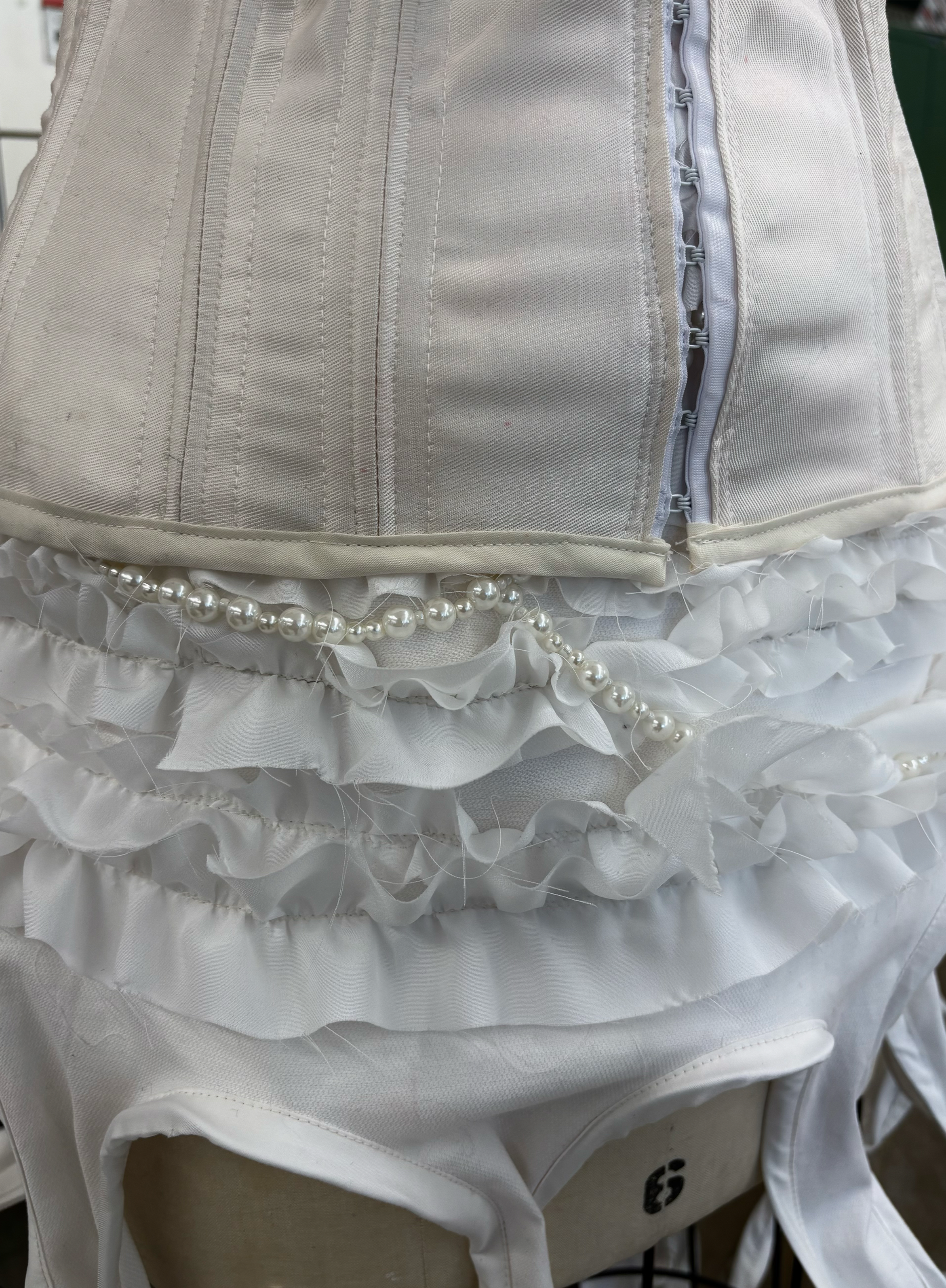 Close-up of a wedding dress with ruffles, pearls, and a zipper.