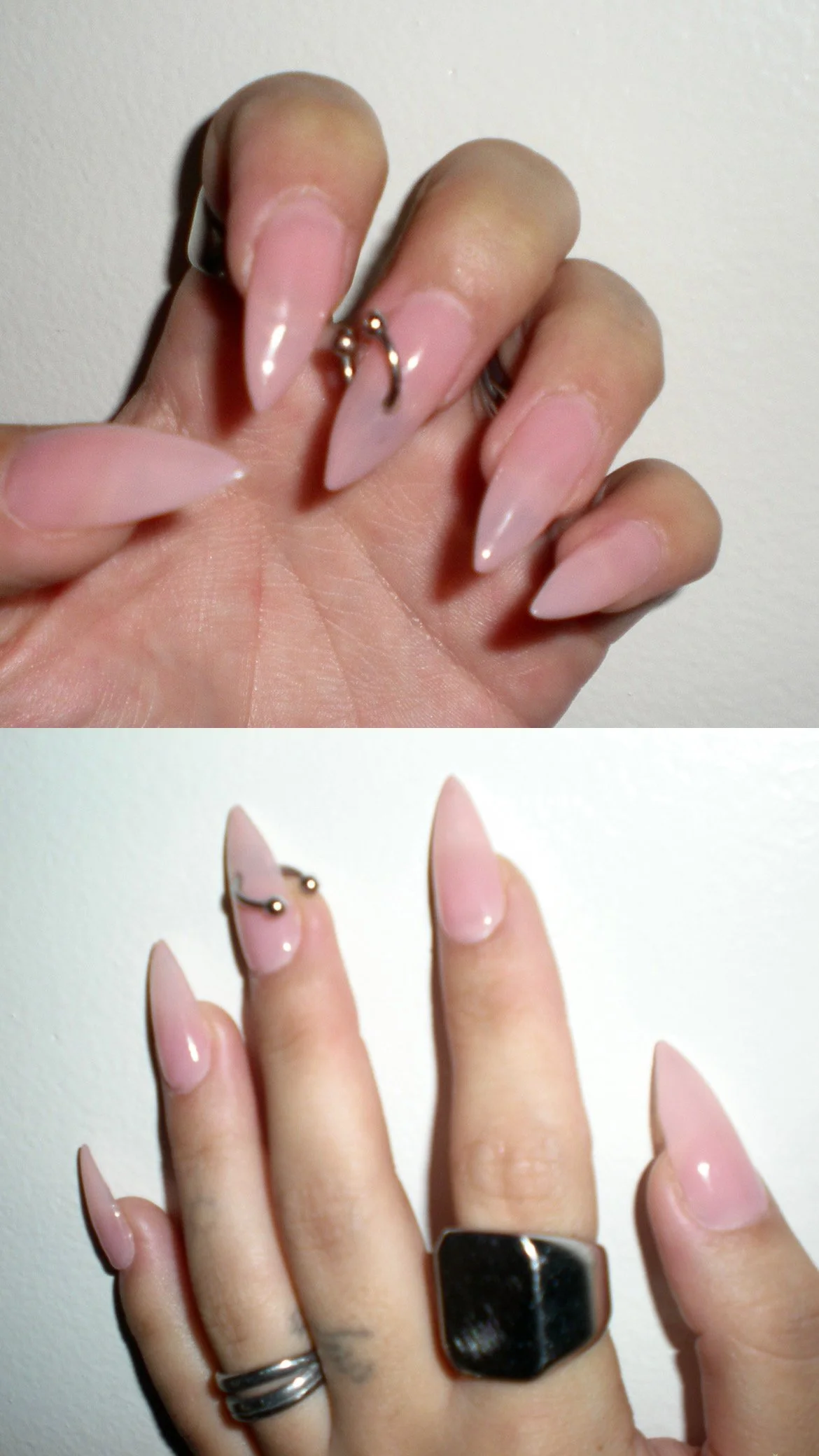 Close-up of a hand with long, pointed, pink acrylic nails, several silver rings, and a tattoo on the middle finger, against a white background.