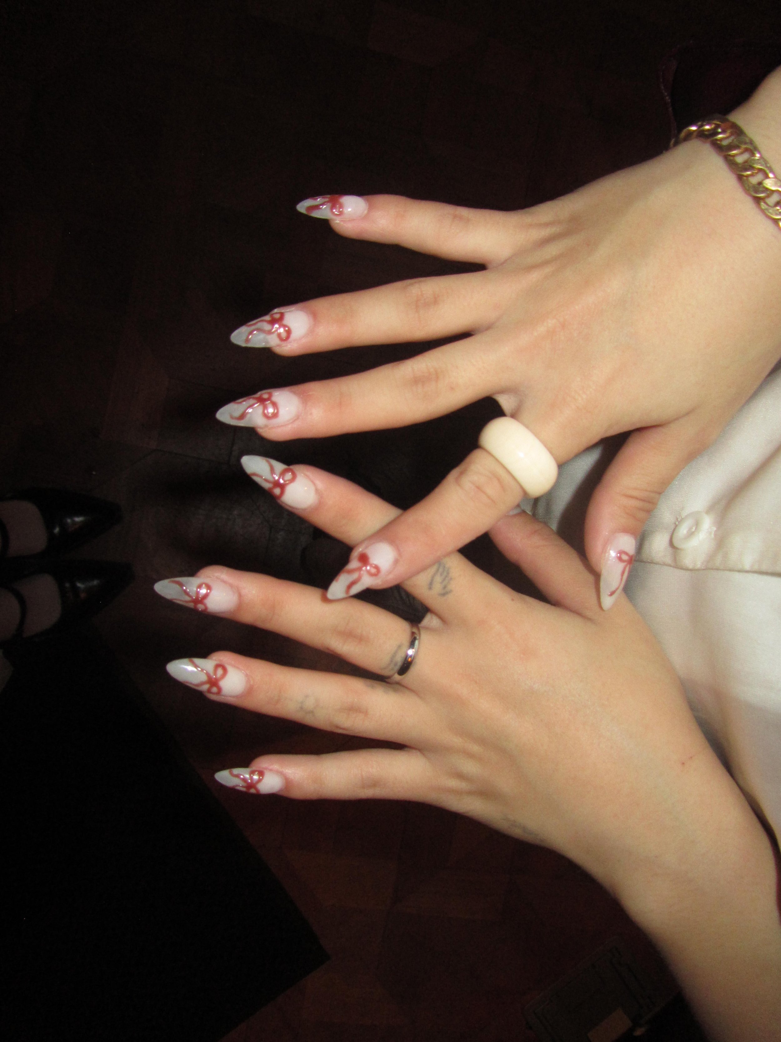 Close-up of a person's hands with manicured nails featuring white and red nail art, adorned with rings and a gold chain bracelet.