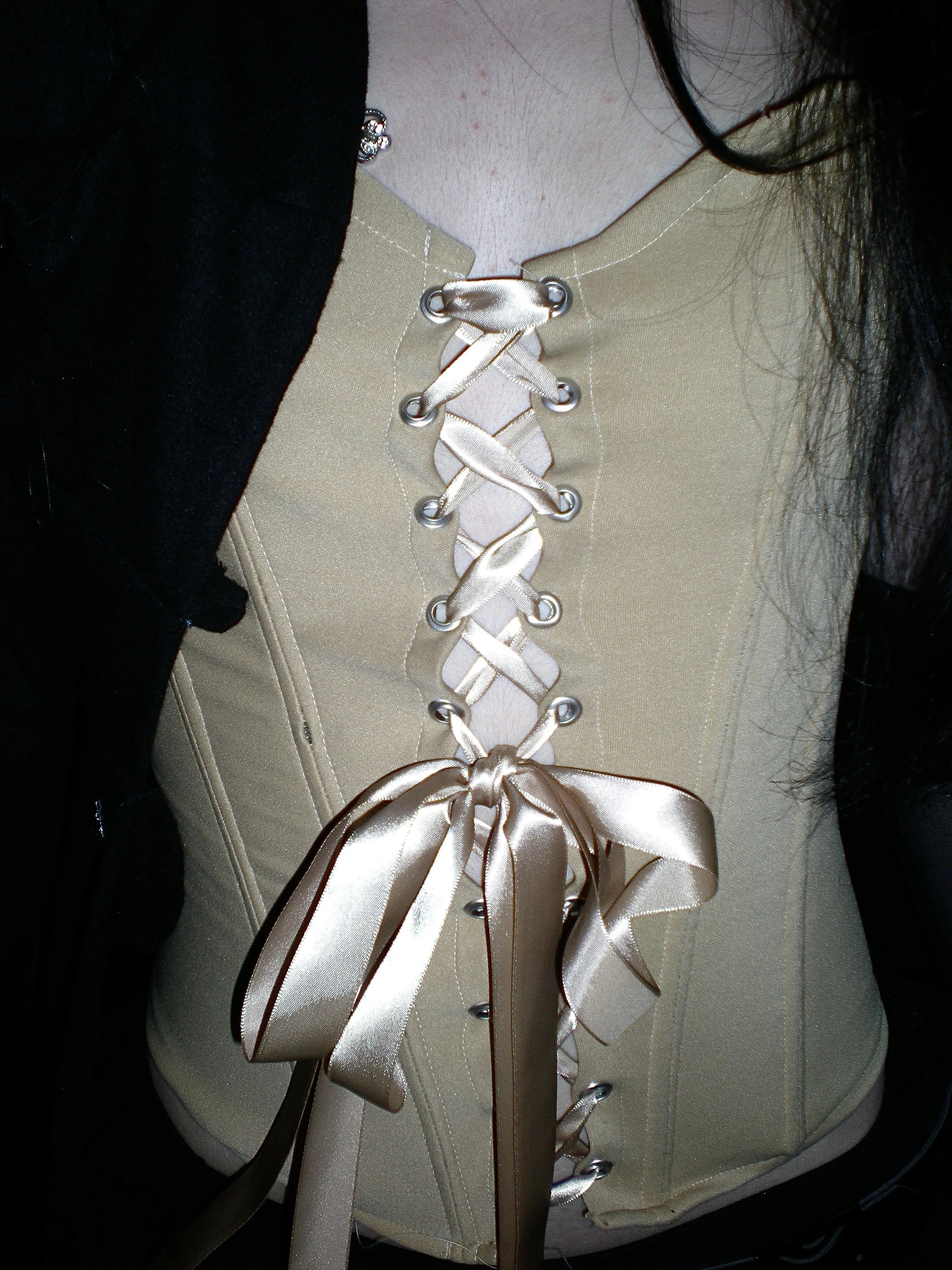 Close-up of a beige corset with a satin ribbon laced through metal eyelets, tied in a bow at the bottom.