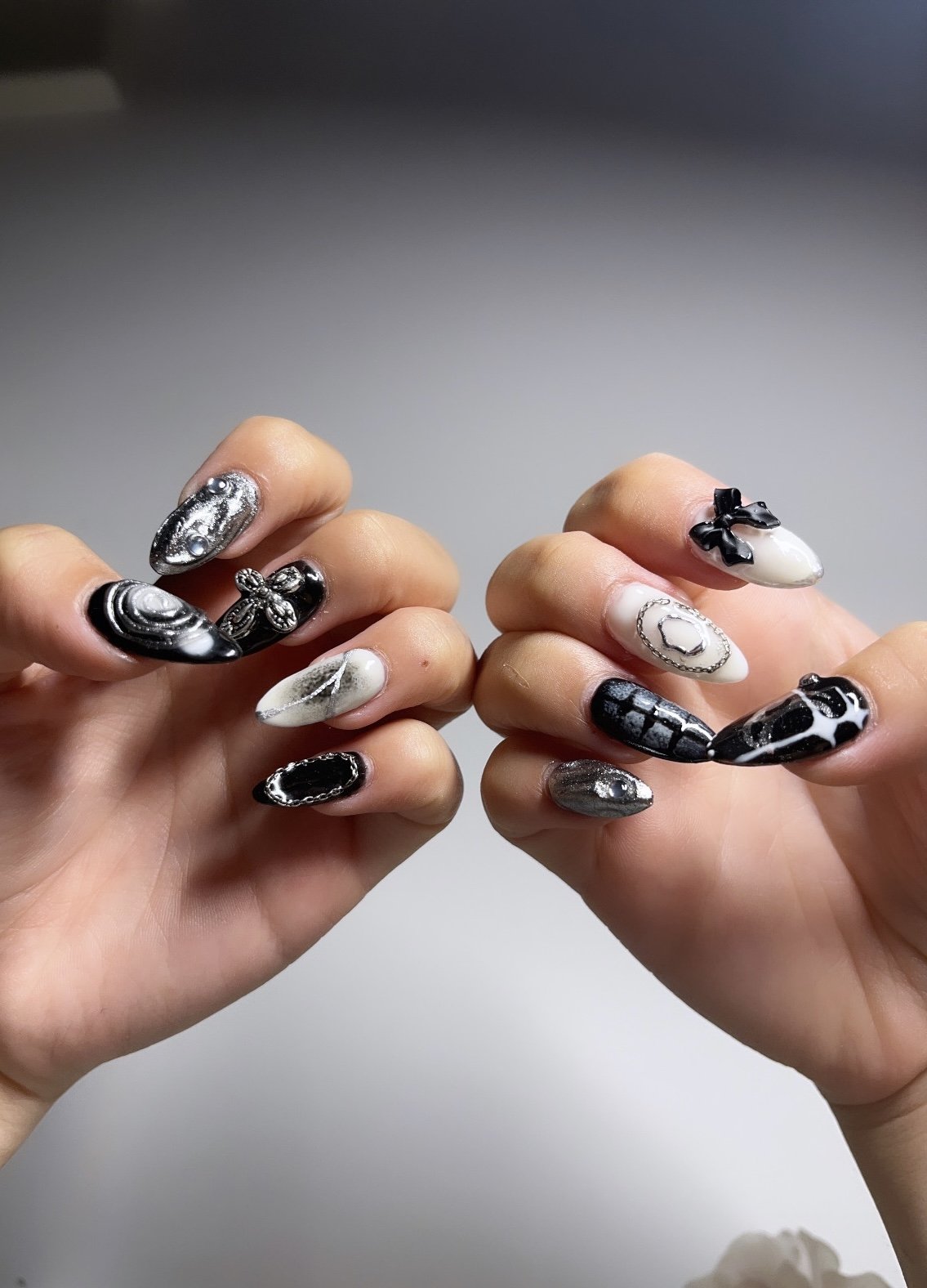Close-up of hands with black and white marbled, metallic, and graphic patterned nail art, featuring embellishments and various designs.