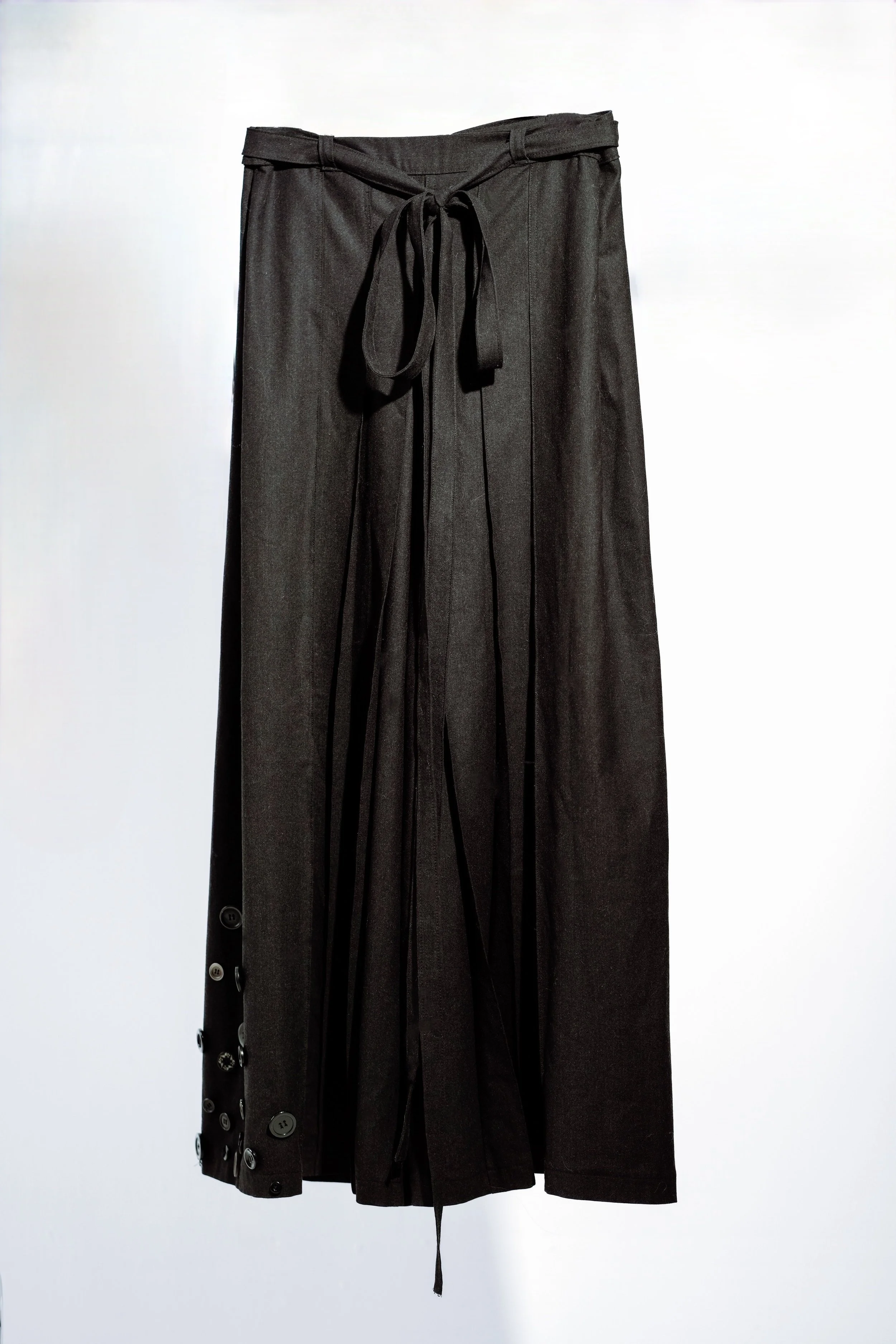 Black high-waisted skirt with a wrap-around tie, button details on the side, hanging against a plain background.