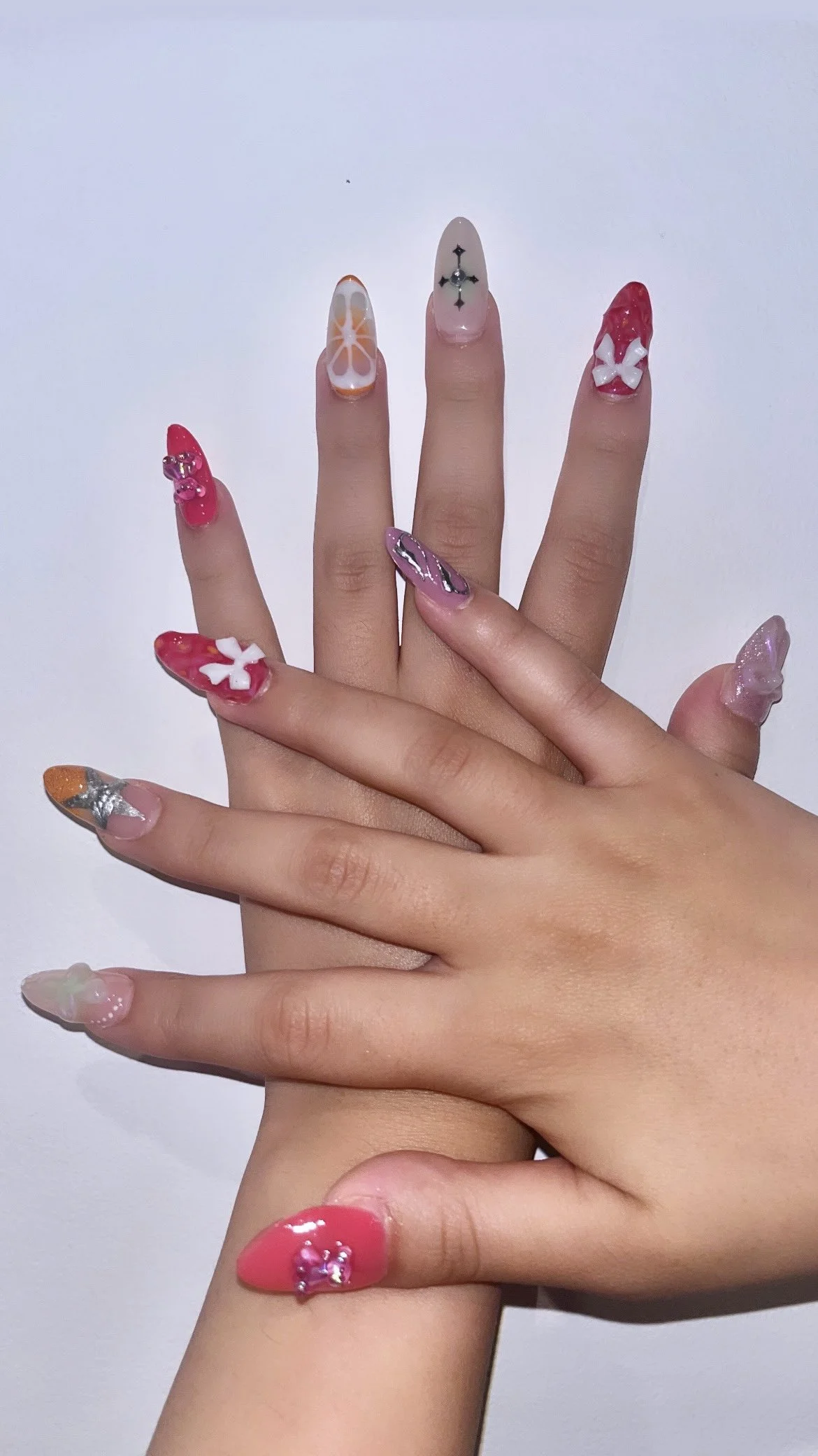Close-up of two hands with colorful, decorated acrylic nails featuring various designs and 3D embellishments.