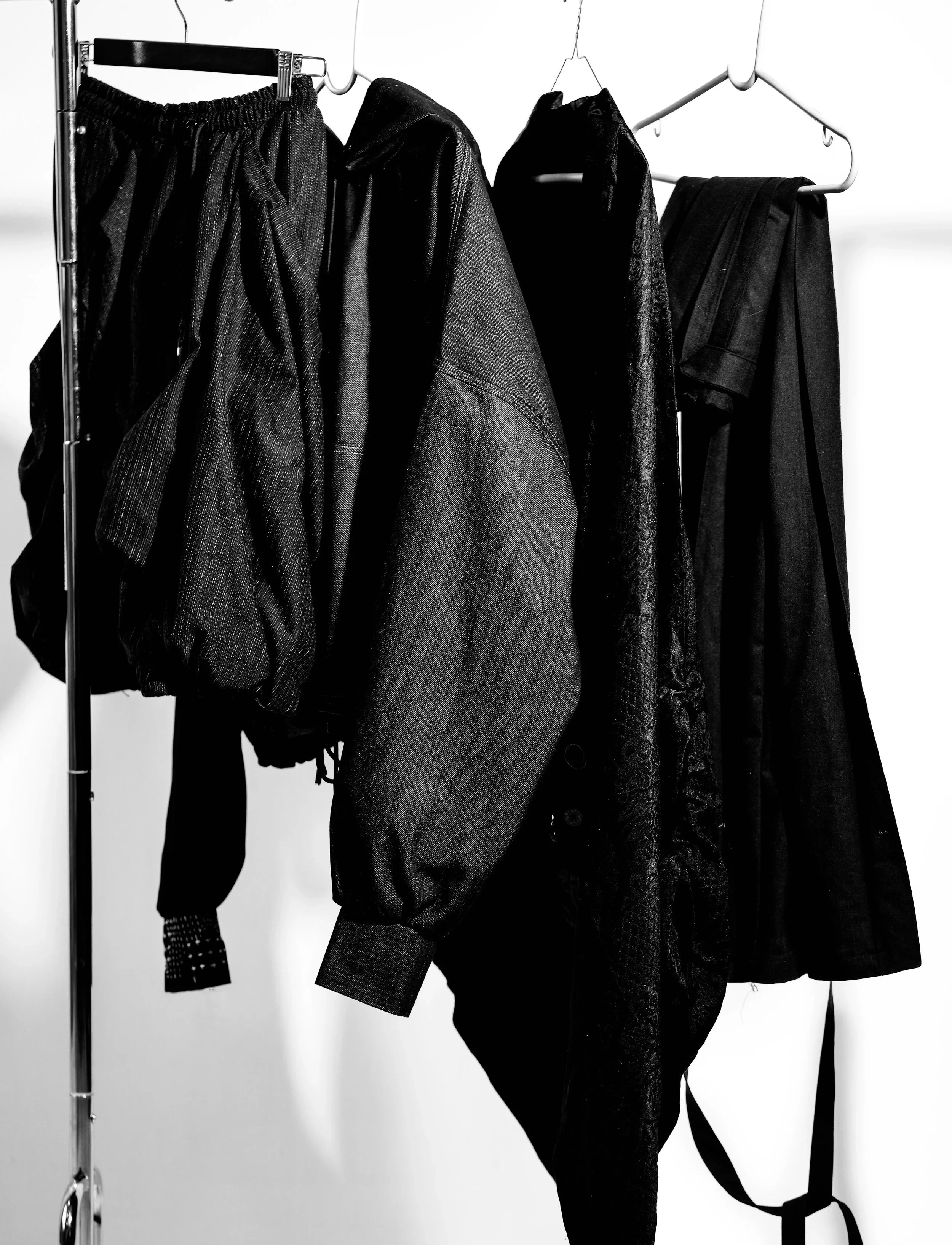 Black jackets and pants hanging on a metal clothing rack against a white background.