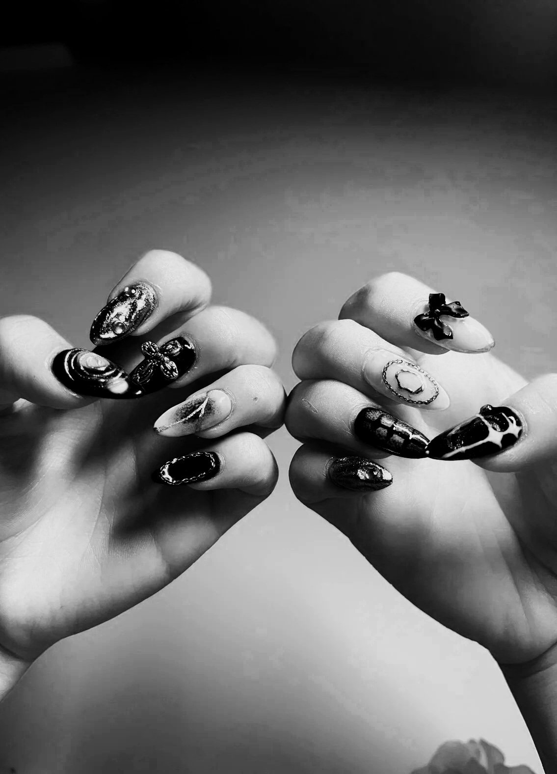 Close-up of hands with decorated nails featuring various designs, some with 3D embellishments, in black and white.
