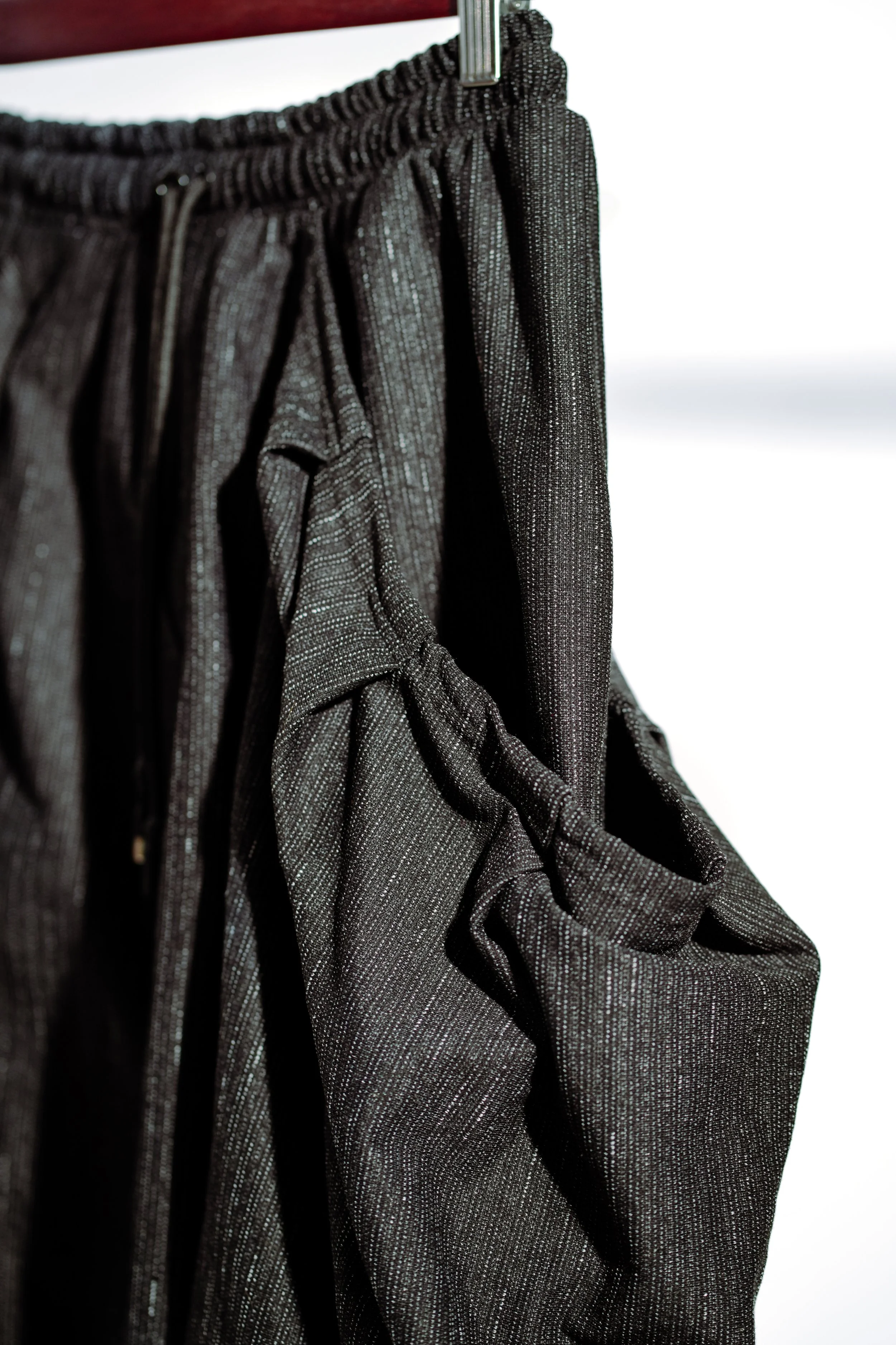 Close-up of a shiny black pair of pants hanging on a hanger against a white background.