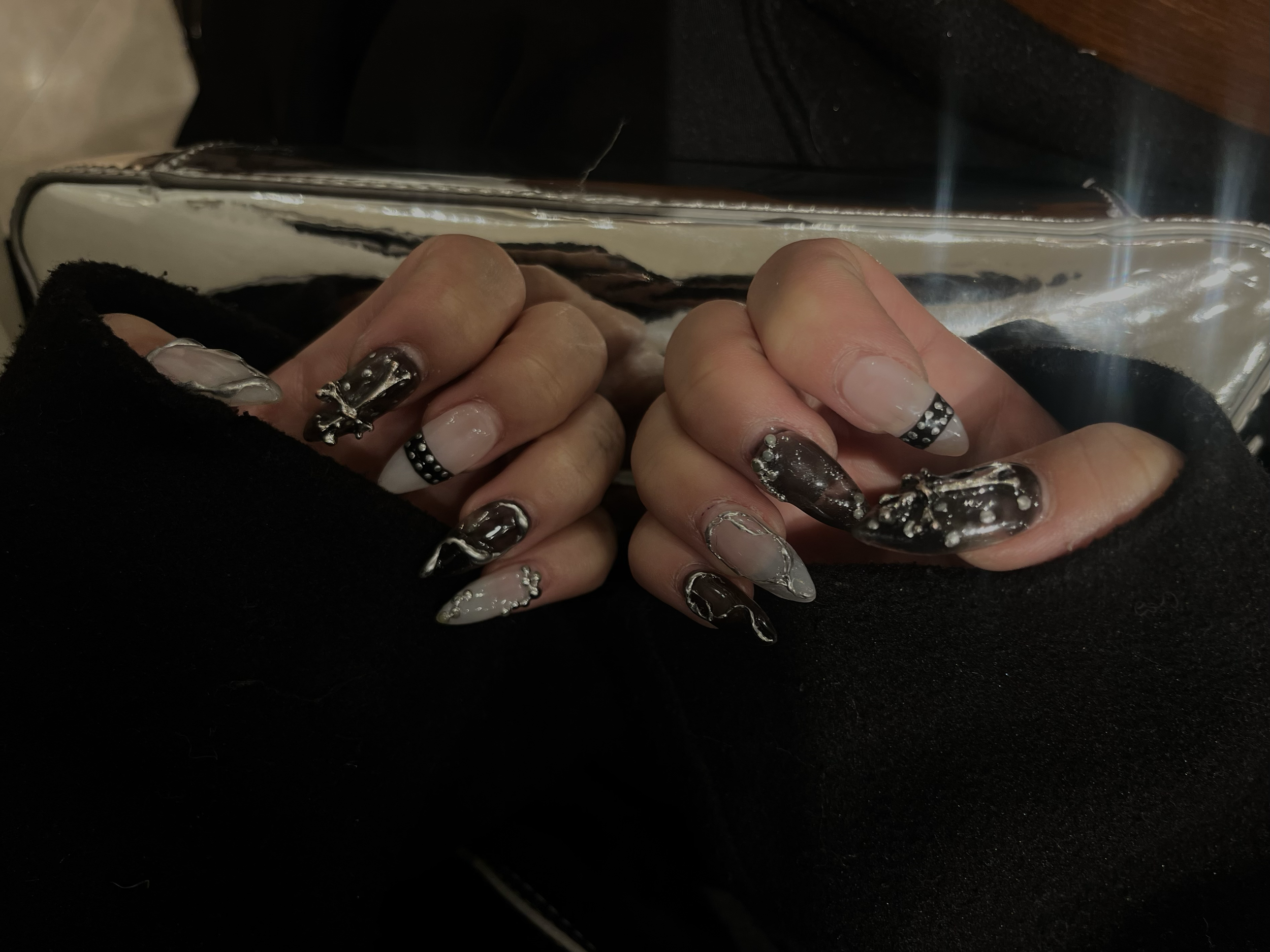 Close-up of hands with black, white, and silver marble-nail art. The nails are decorated with rhinestones and metallic accents.