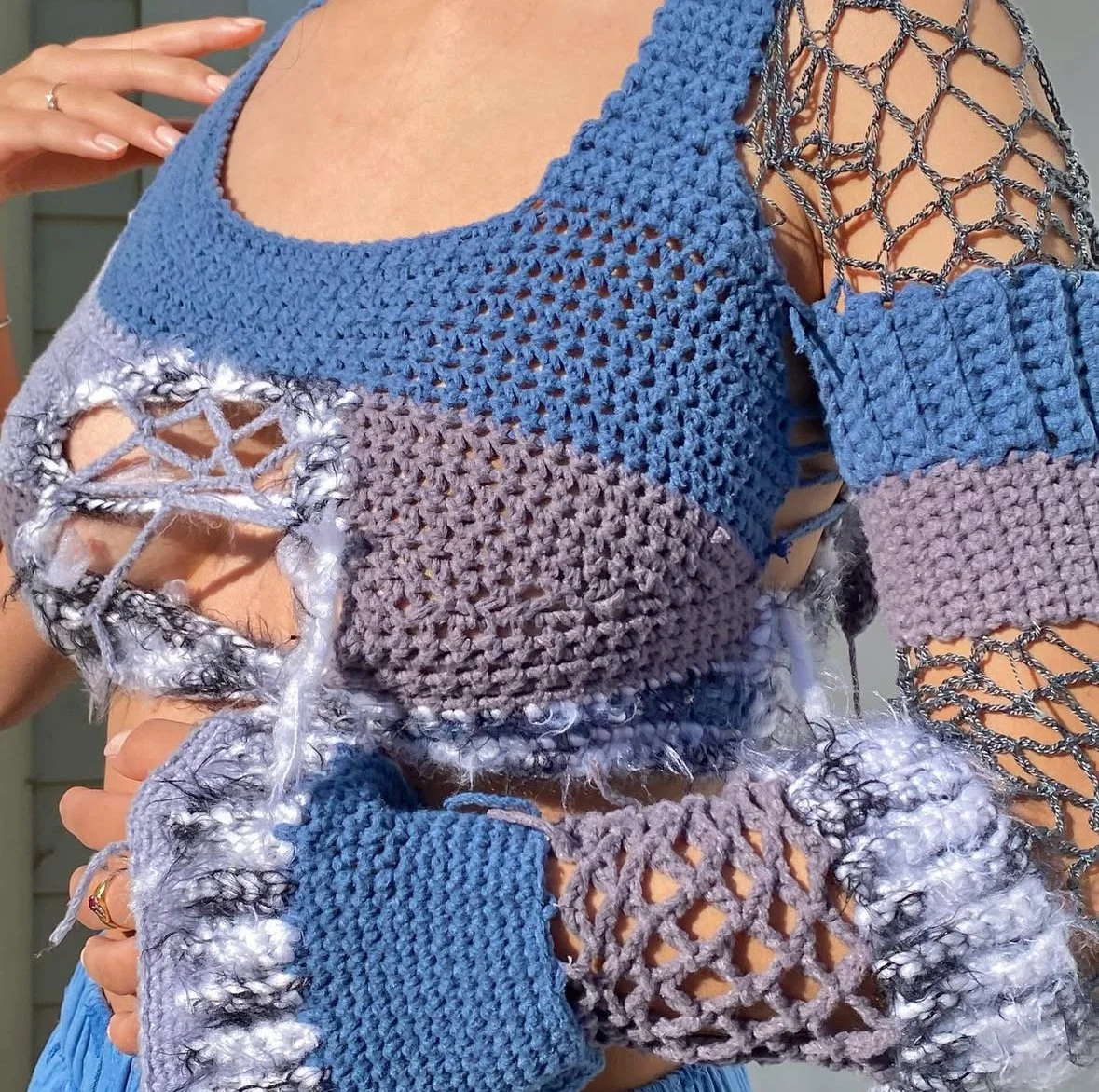 Close-up of a person wearing a handmade, multi-colored crochet sweater with open-knit and chain-link details on the sleeves.