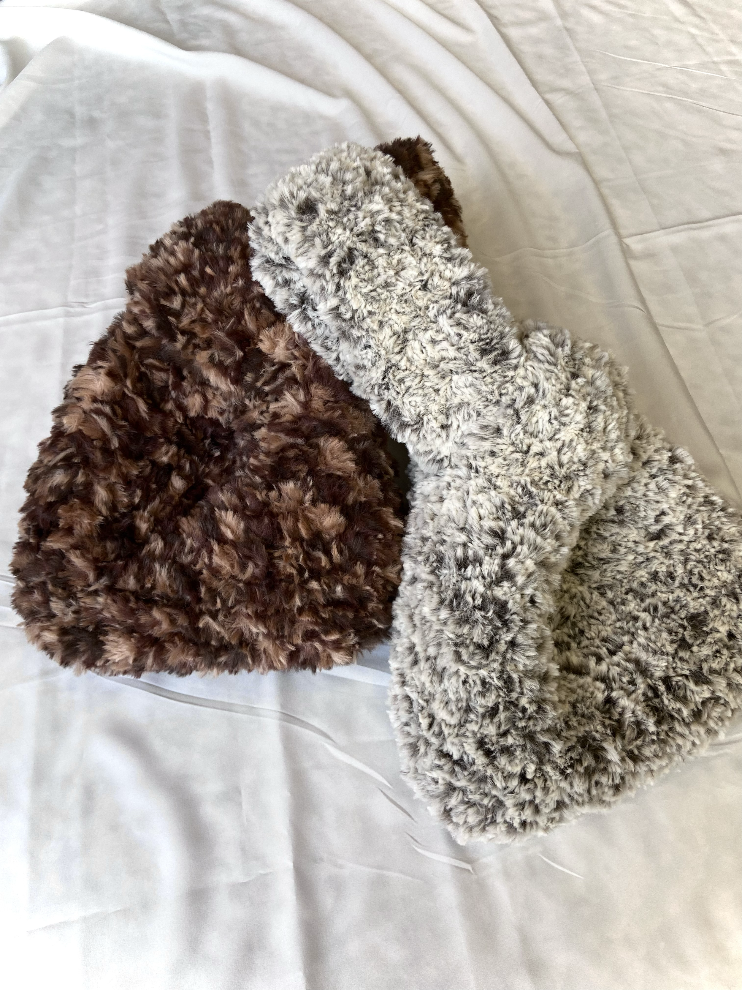 Two fluffy, textured rectangular objects, one brown and one gray, resting on a white fabric background.