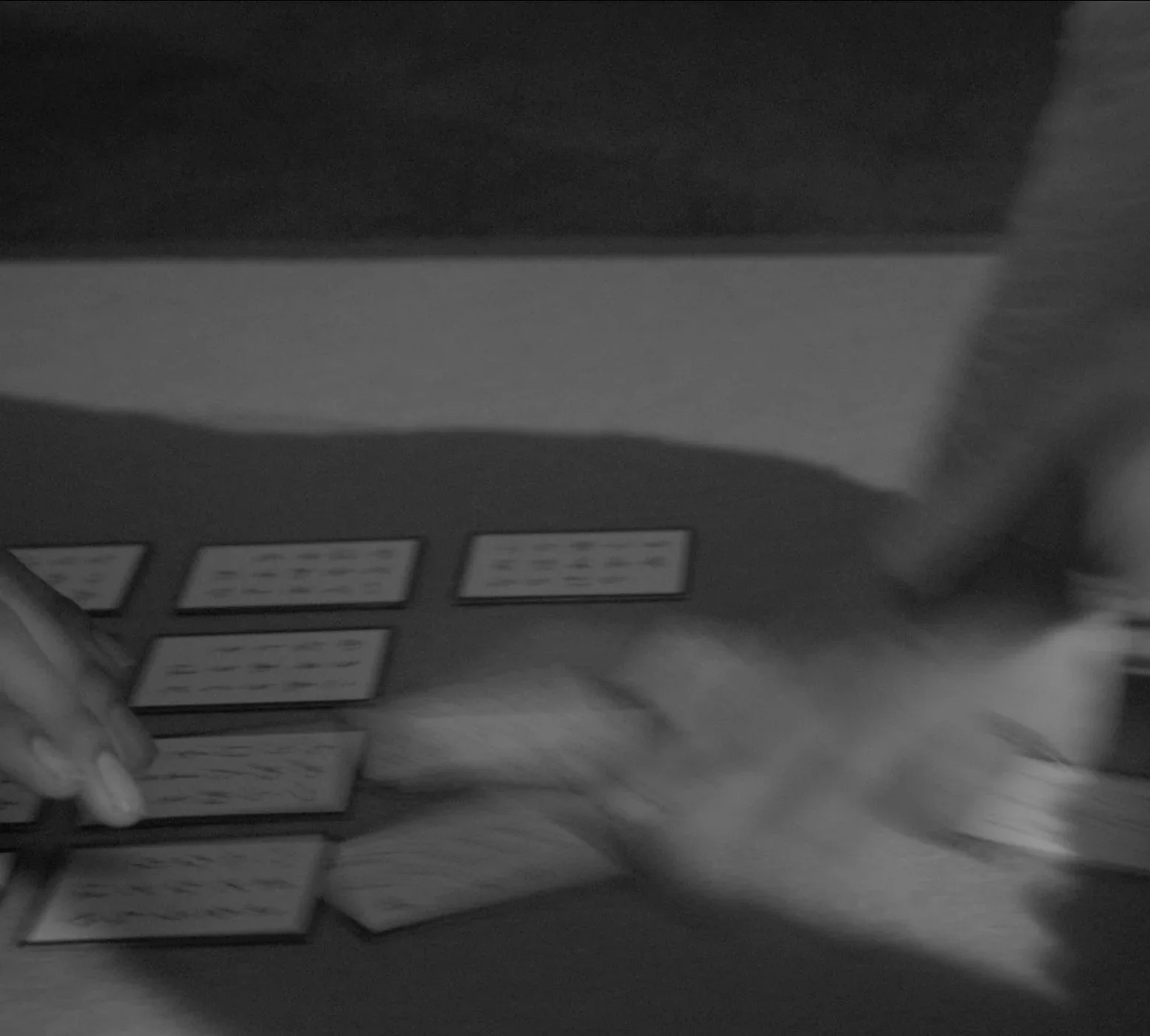 Two people play a card game at a table in a black-and-white photo, with several playing cards spread out on the table.