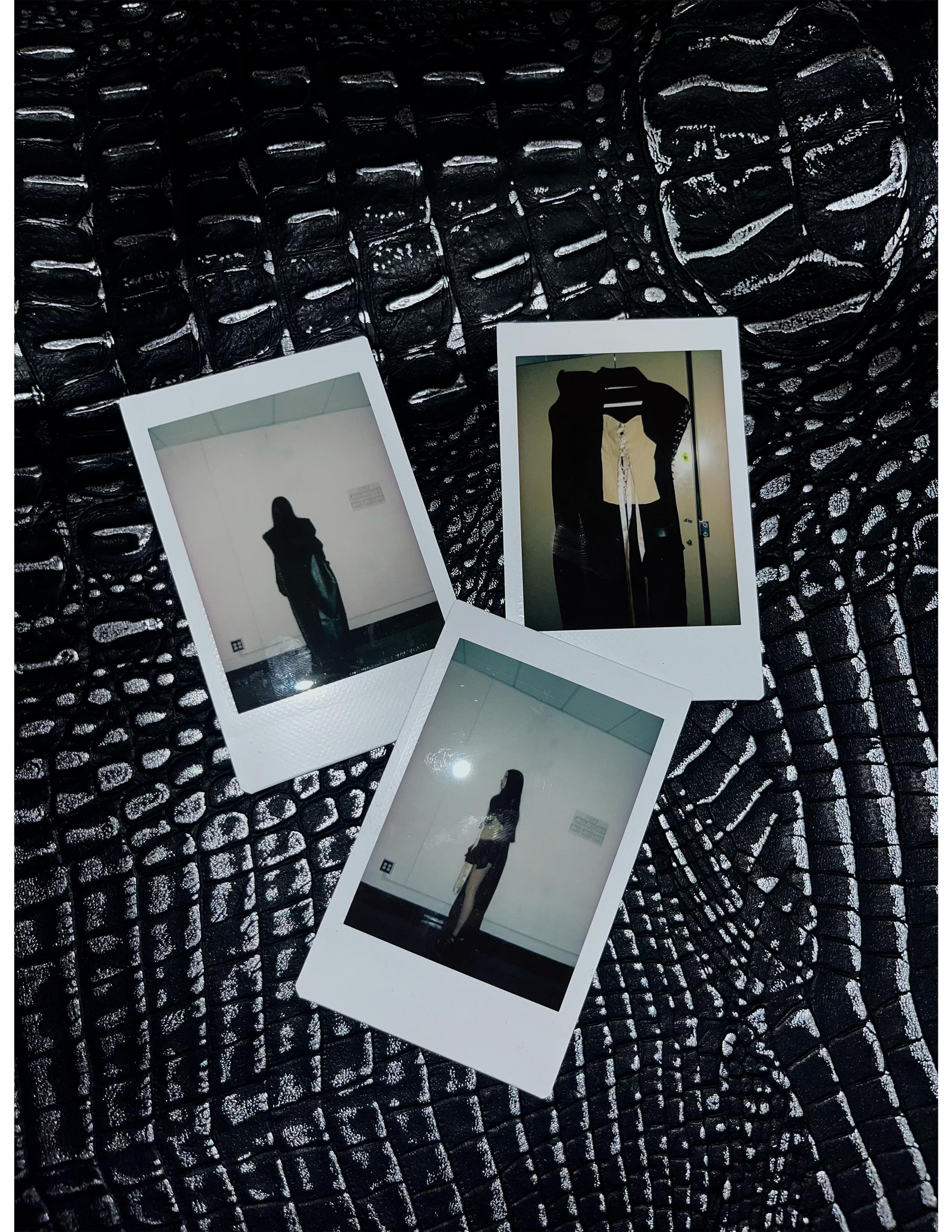 Three Polaroid photos on a black textured surface. The photos show silhouettes of a person standing against a plain background, and one shows a clothing rack with dresses.
