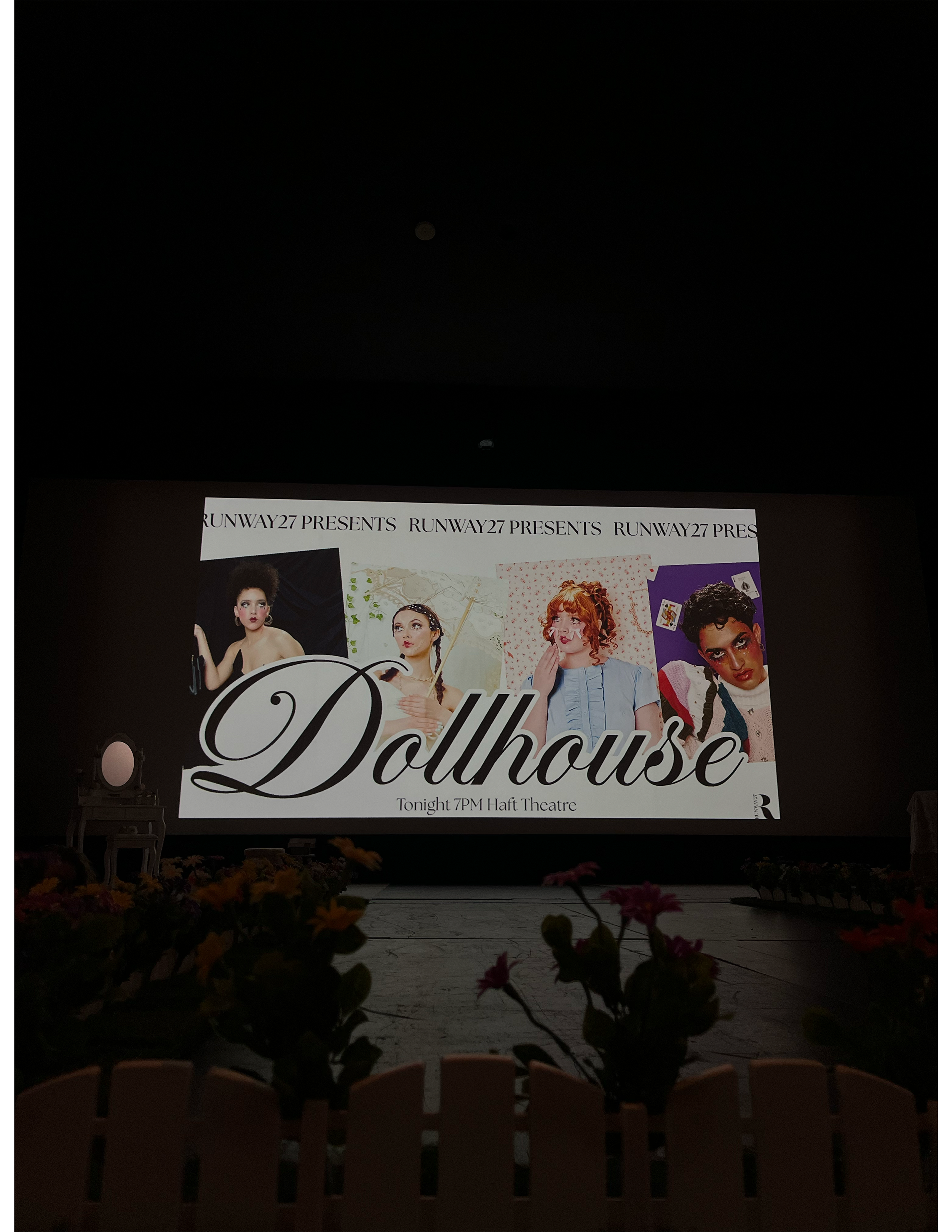 The image shows a dark theater with a large screen displaying promotional poster for the play 'Dollhouse,' presented by Runway27, scheduled for tonight at 7 PM at Haft Theatre. The poster features four women in different poses and outfits.
