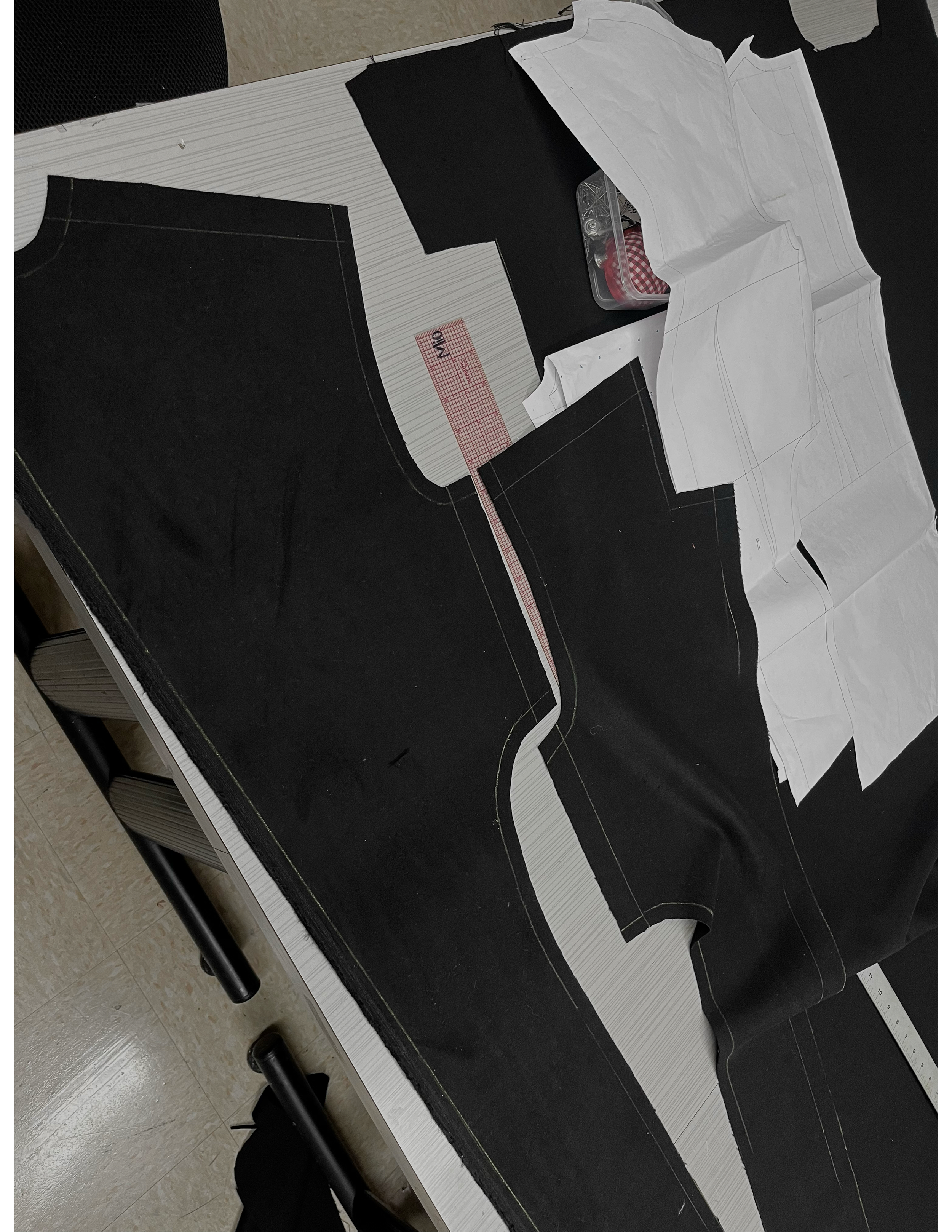 Pattern pieces and fabric for garment sewing laid out on a table, with tools and markings visible.