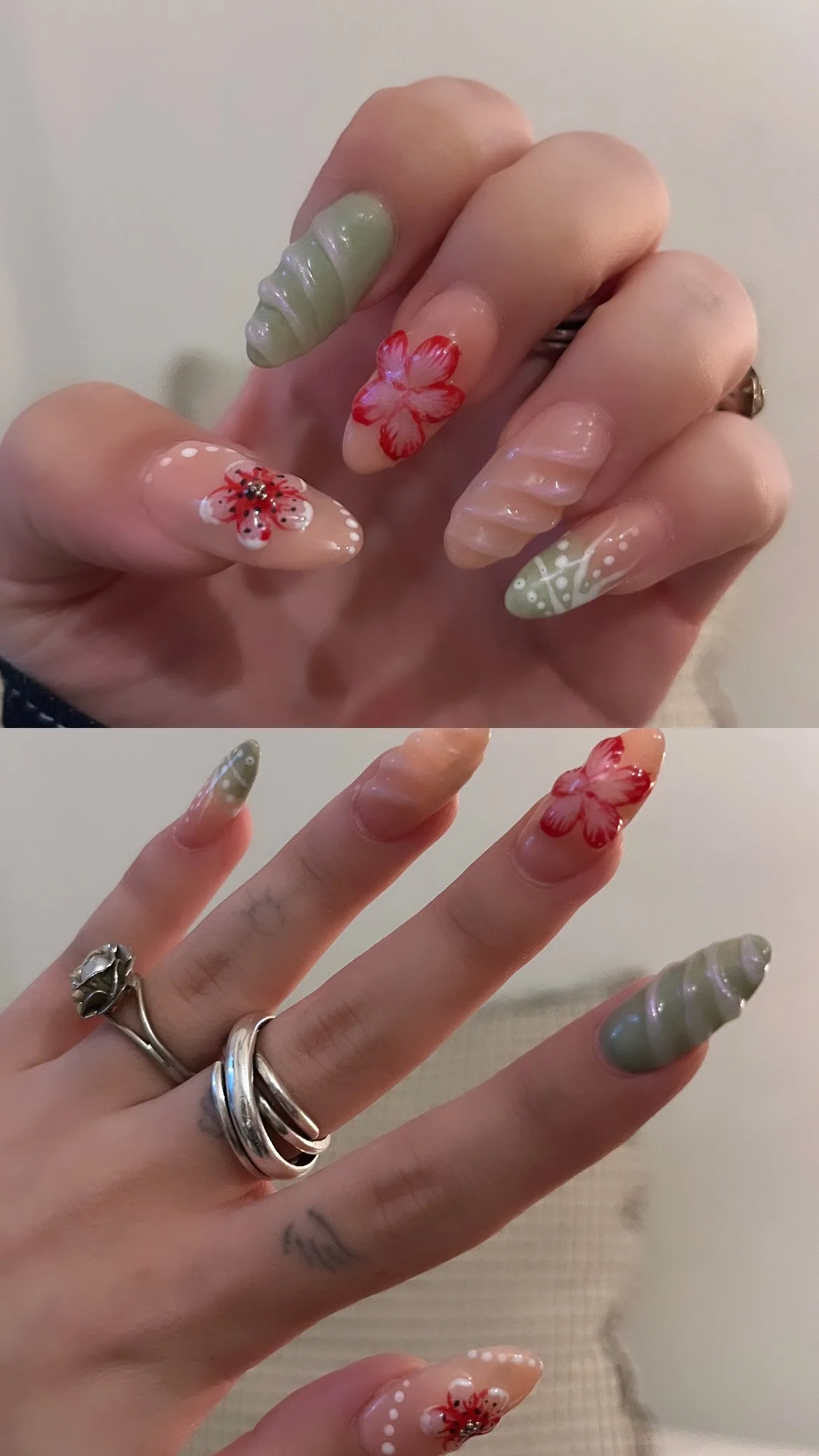 Close-up of a hand with long, decorated nails featuring floral and abstract designs in pink, white, green, and beige. The hand is adorned with multiple rings, including one with a flower design. The background is a soft, neutral color.
