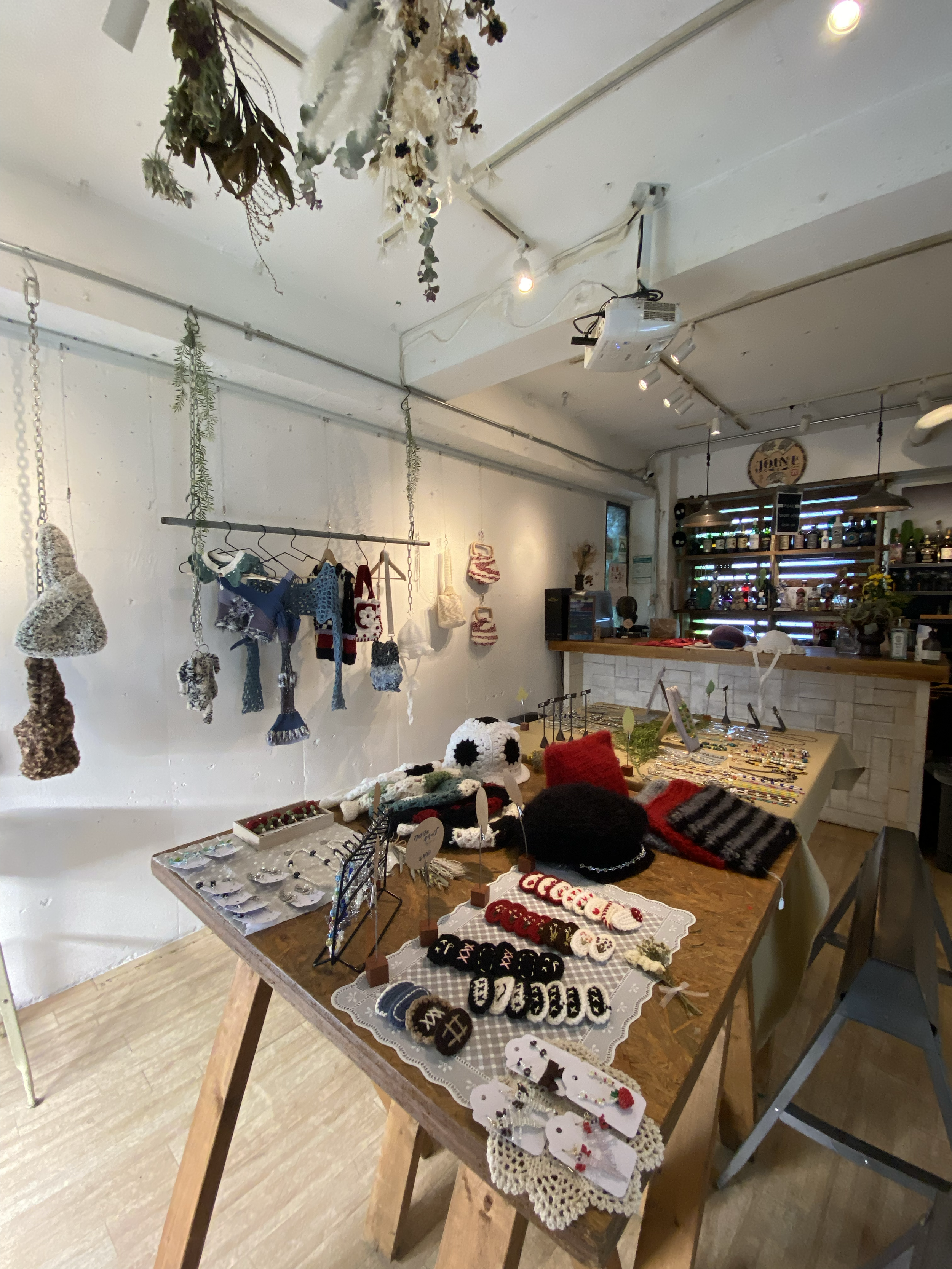 A display of handmade crafts including knitted and crocheted items such as hats, ornaments, and jewelry on a wooden table inside a cozy shop.