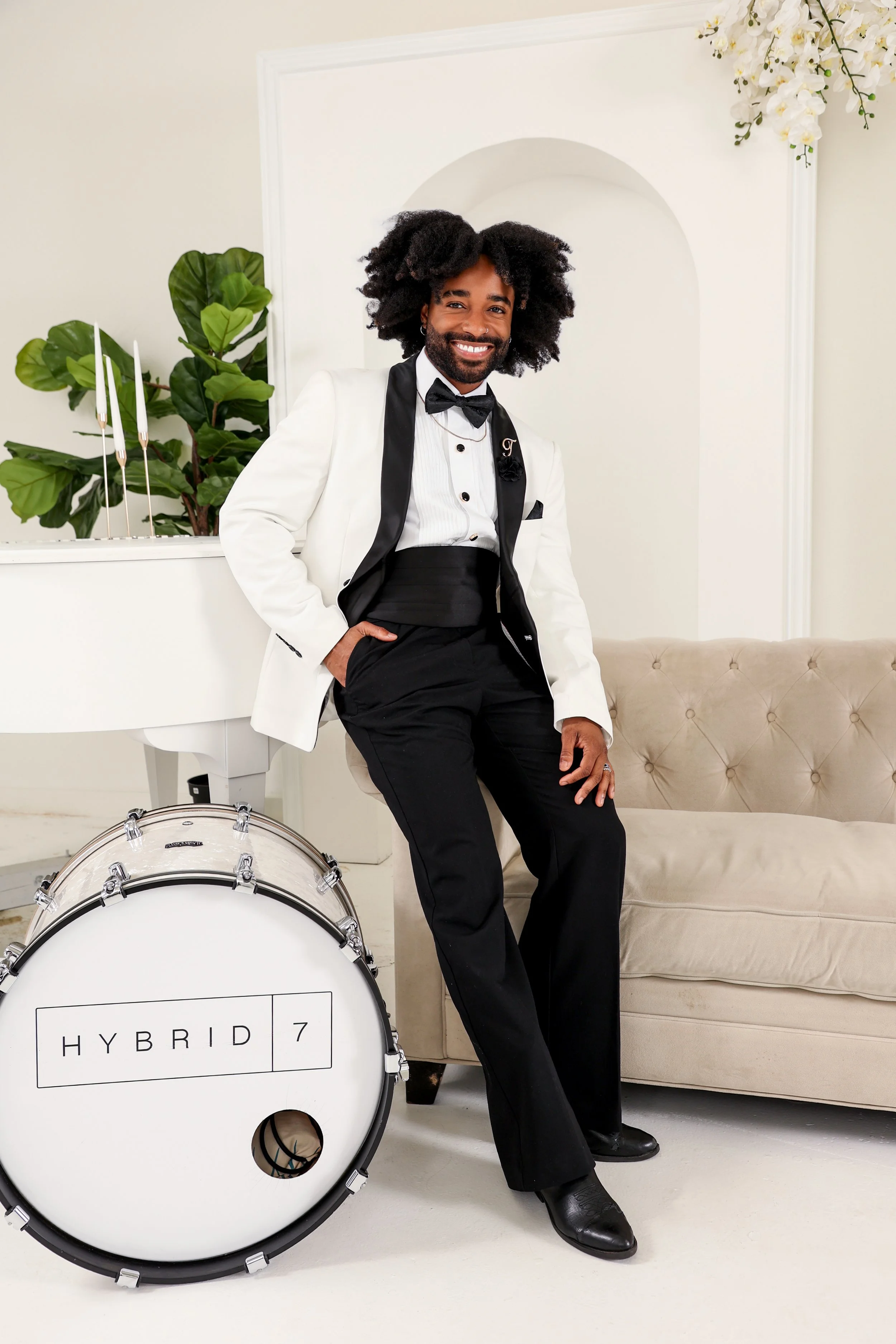 A newlywed couple walking arm-in-arm down a grassy aisle surrounded by friends and family throwing confetti at their outdoor wedding ceremony. The bride is in a white gown, and the groom is in a light gray suit. A wooden wedding arch decorated with flowers is behind them, with a mountain landscape in the background.