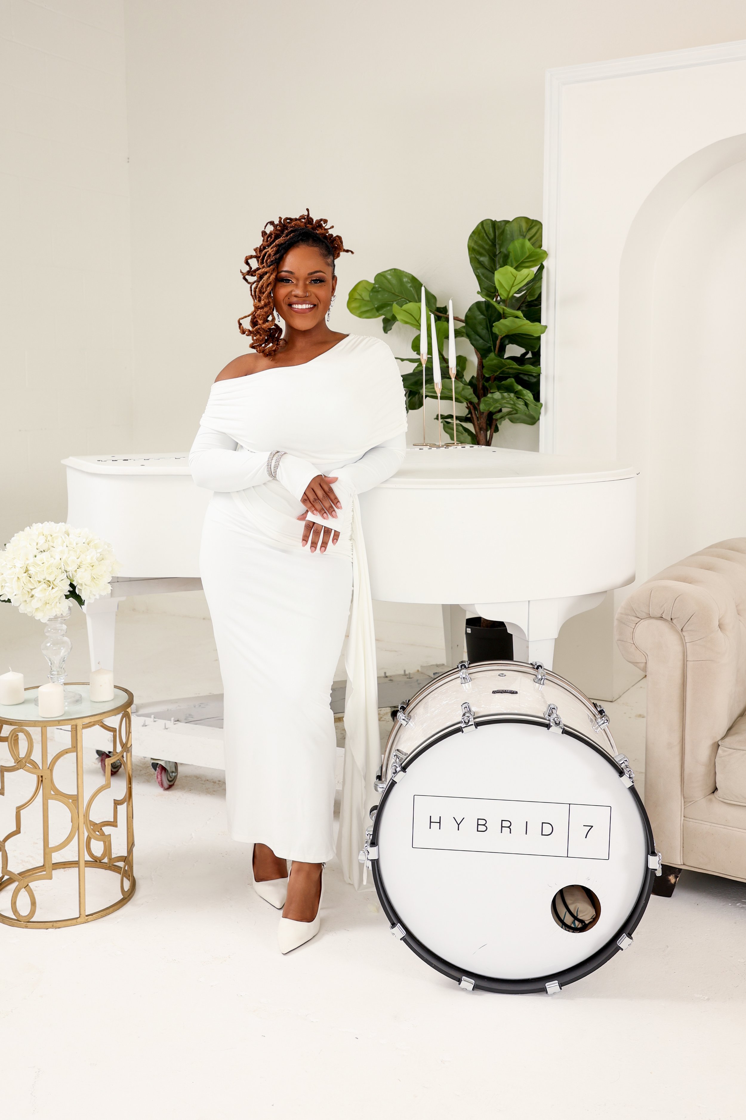 Decorative floral arch in front of a red wooden fence, with white chairs and flower arrangements on the grass.