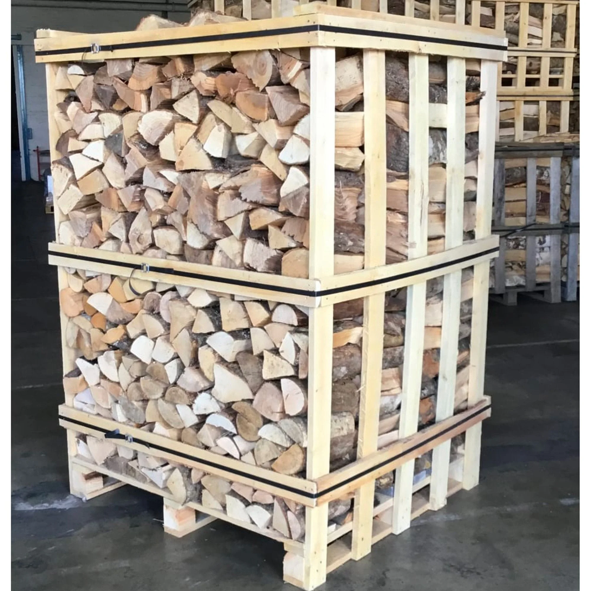 Stacked firewood packed in wooden crates with horizontal black straps in a warehouse.