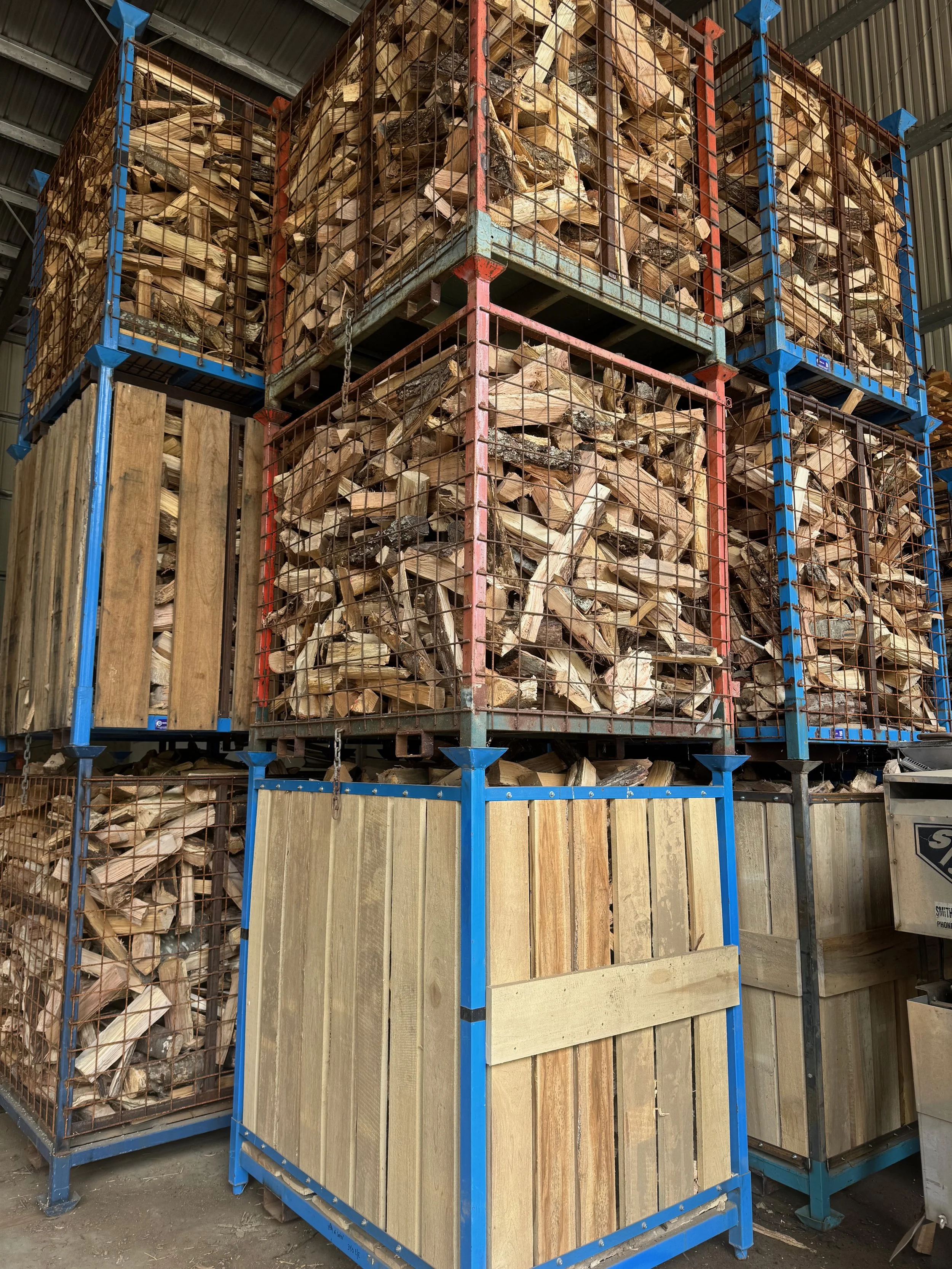 Stacks of firewood stored in metal cages and wooden bins inside a warehouse.