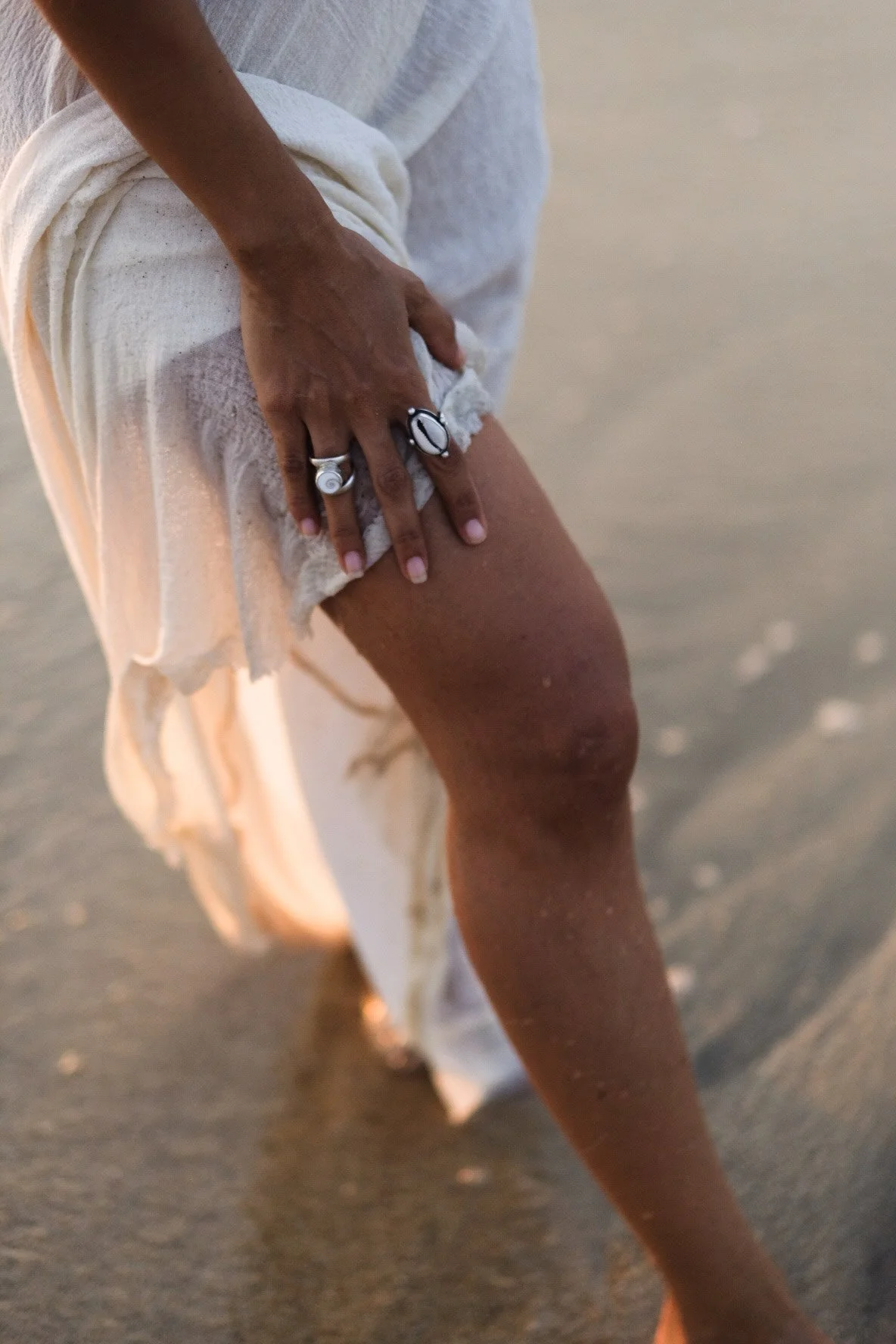 Close-up of a person with dark skin holding onto their thigh with one hand, on a sandy beach.