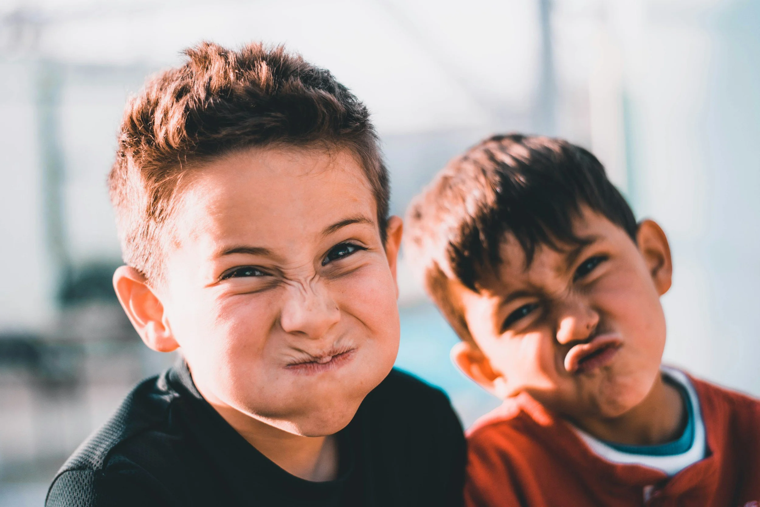 Two young boys making funny faces in a bright indoor setting.