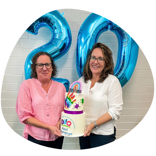 Kendra and Julie hold a cake celebrating 20 yers of Next Challenge