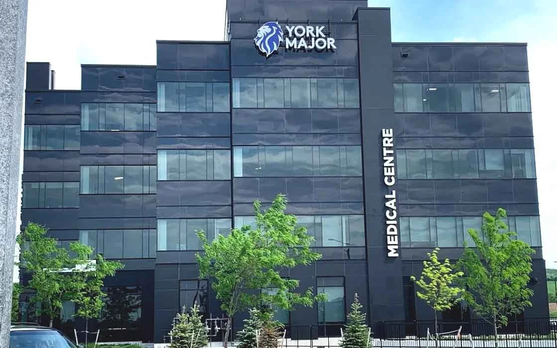 Modern multi-story medical building with glass windows, trees in front, and signs that read 'YORK MAJOR' and 'MEDICAL CENTRE'.
