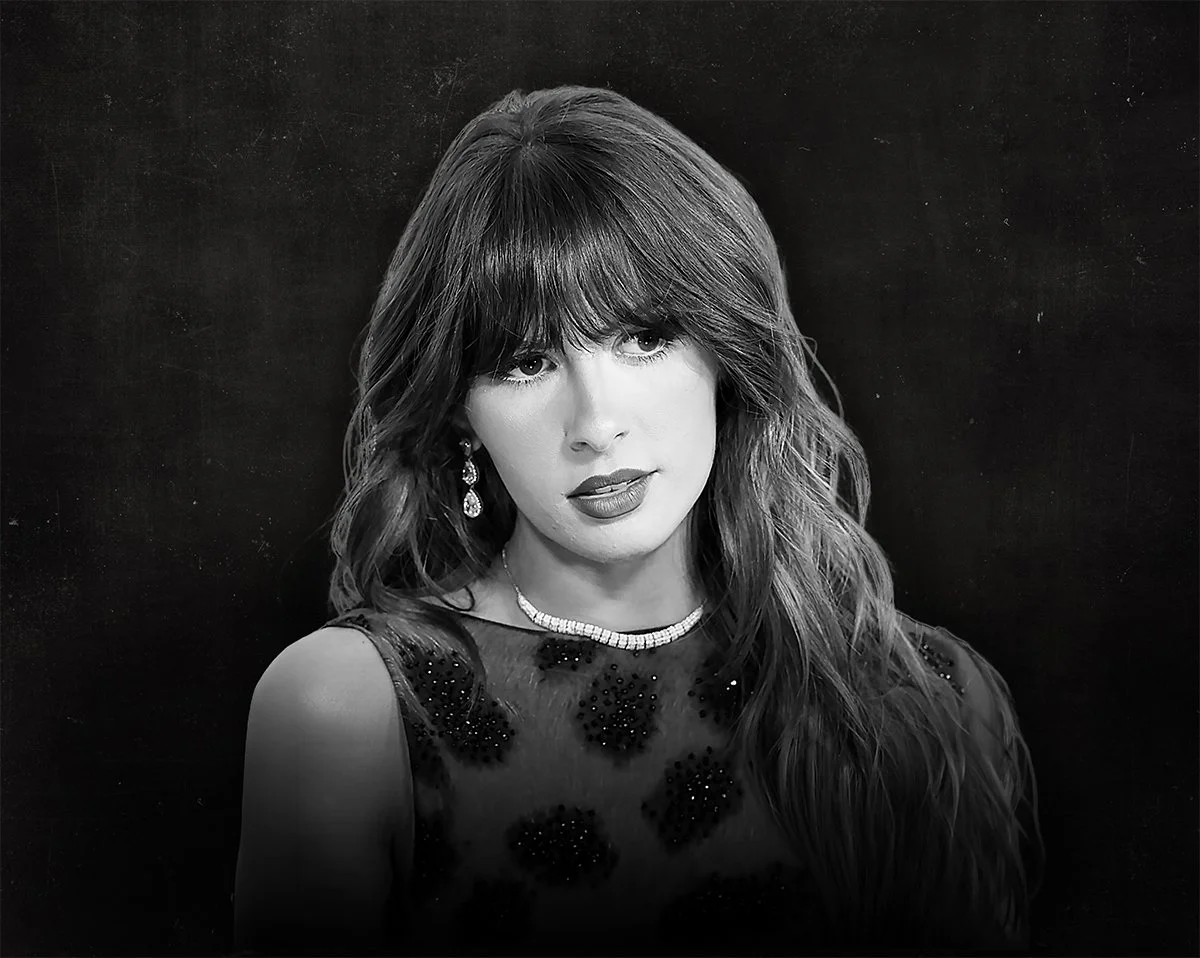 Black and white portrait of a woman with long wavy hair wearing a sequined dress, earrings, and a necklace, standing against a dark background.