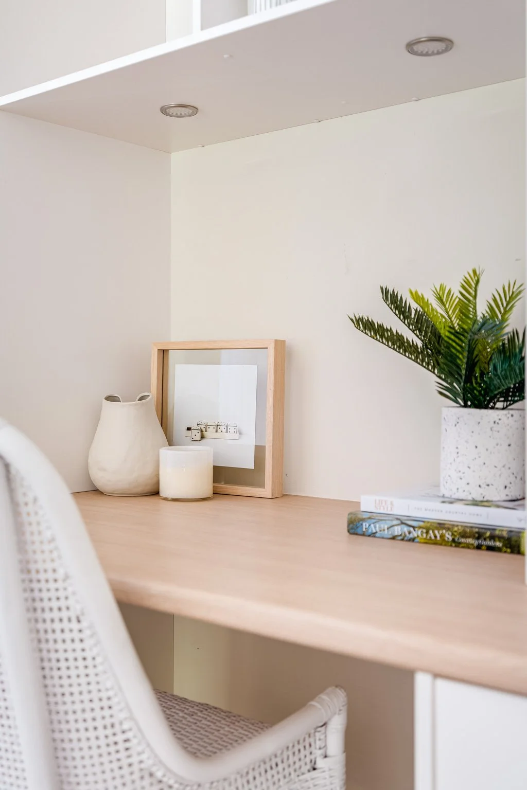 Decorative shelf with a potted plant, framed mirror, candles, and books in a minimalist interior setting.