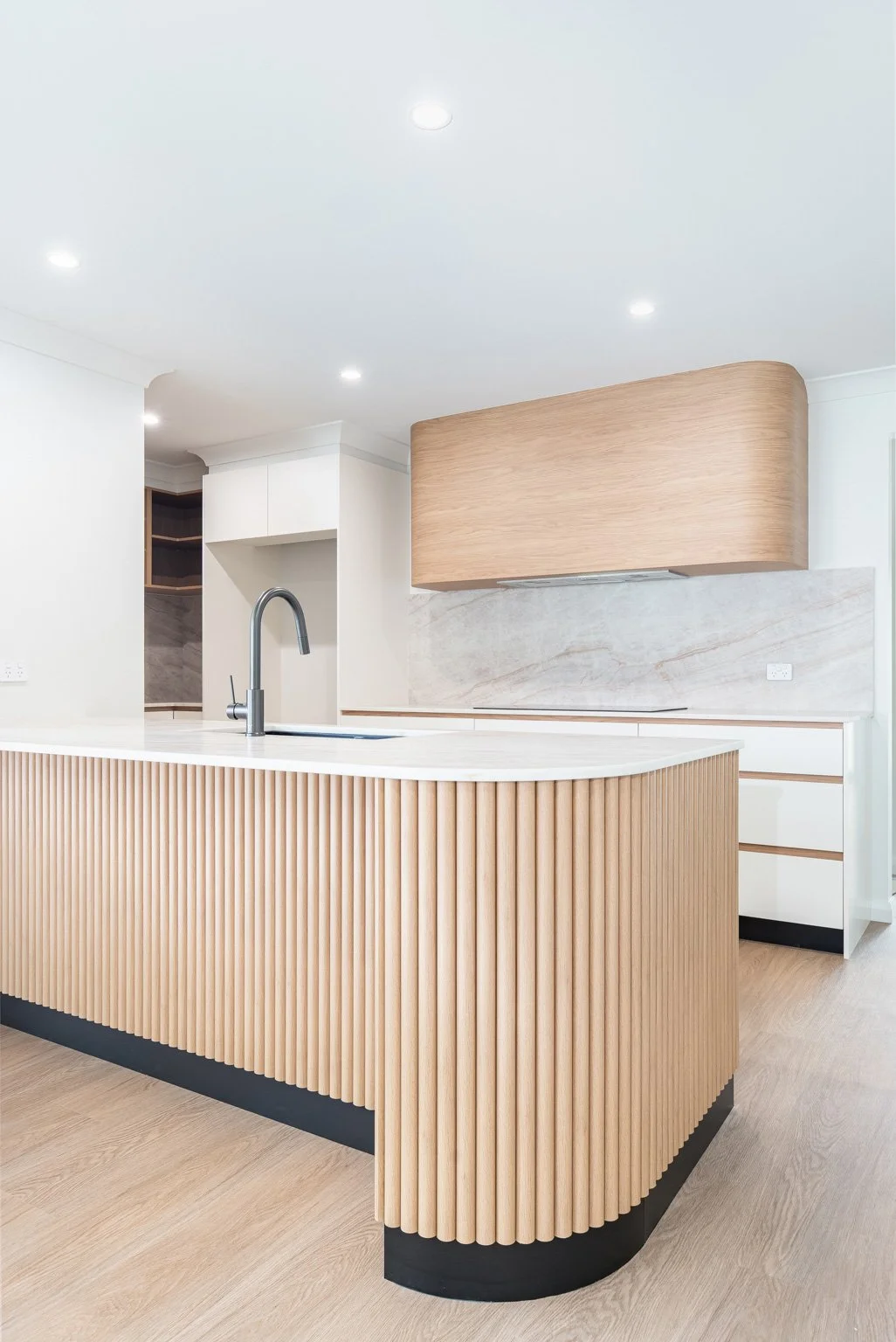 Modern kitchen with wooden island and white cabinets, featuring a built-in sink, minimalist design, light wood flooring, and subtle lighting.
