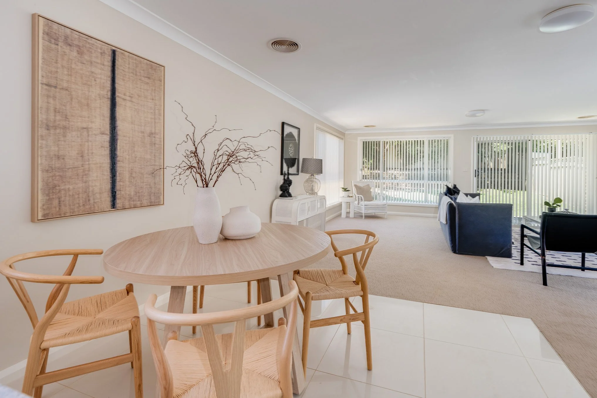 Living and dining room area with beige walls, wooden furniture, and large windows with vertical blinds.