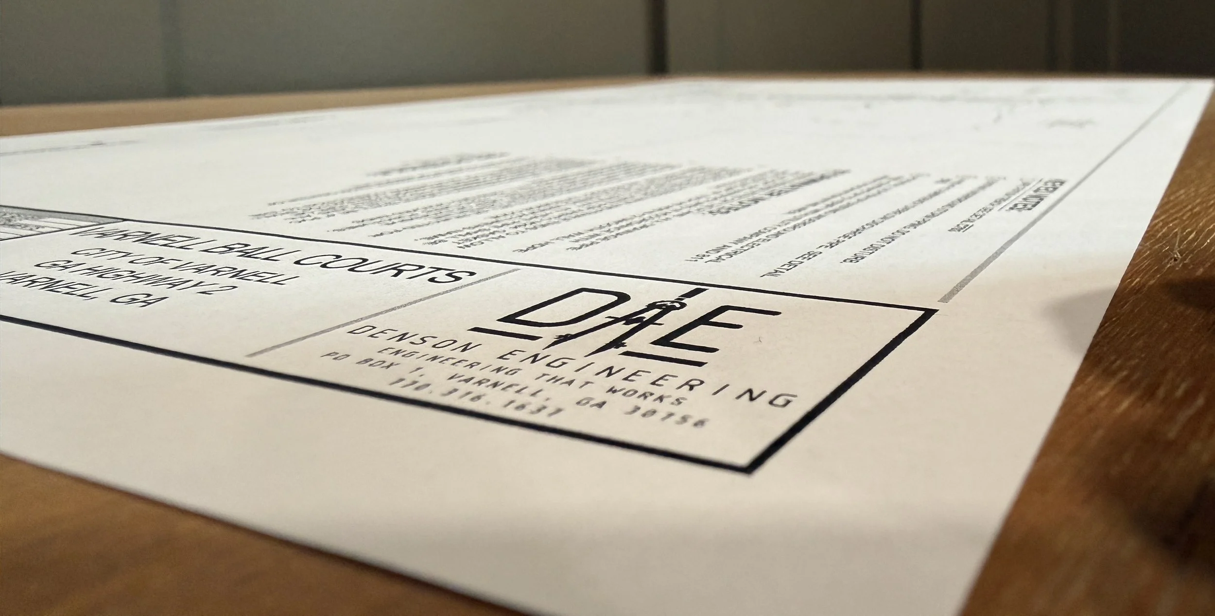 Close-up of a paper on a wooden surface, displaying a Denson Engineering Logo.