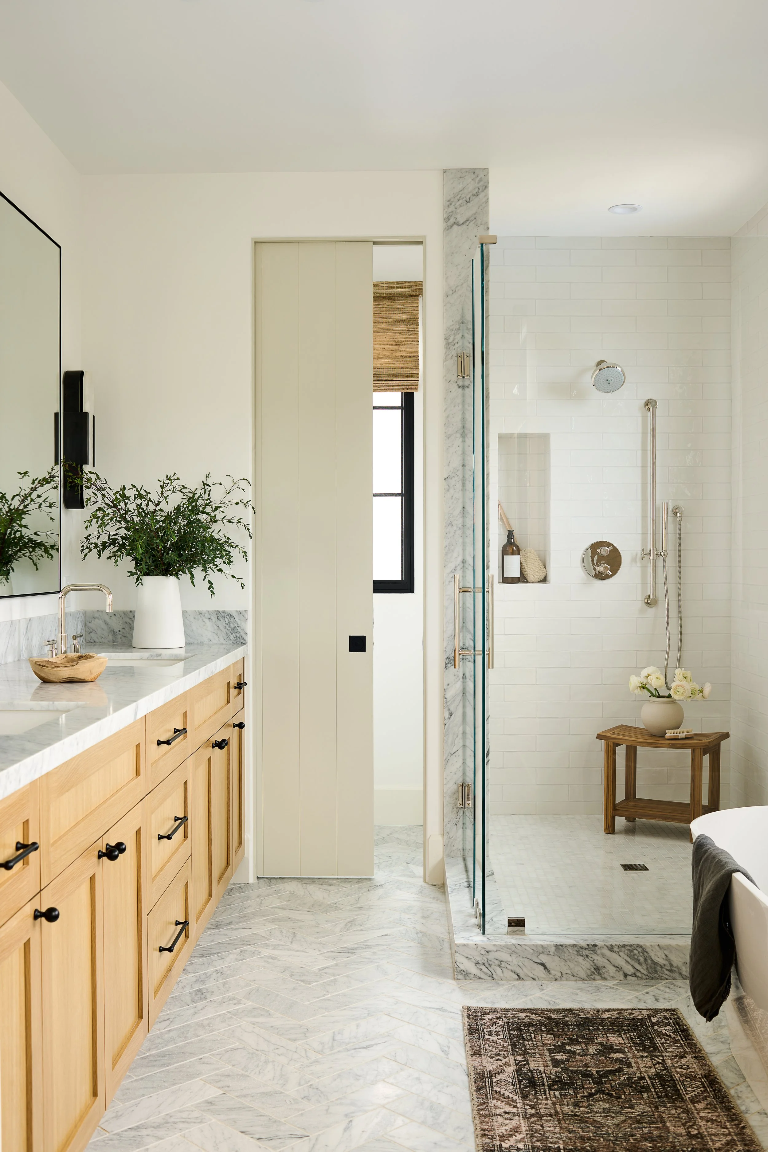 A modern bathroom with a double sink vanity, plants in white vases, a marble countertop, and a separate shower area with white subway tiles.