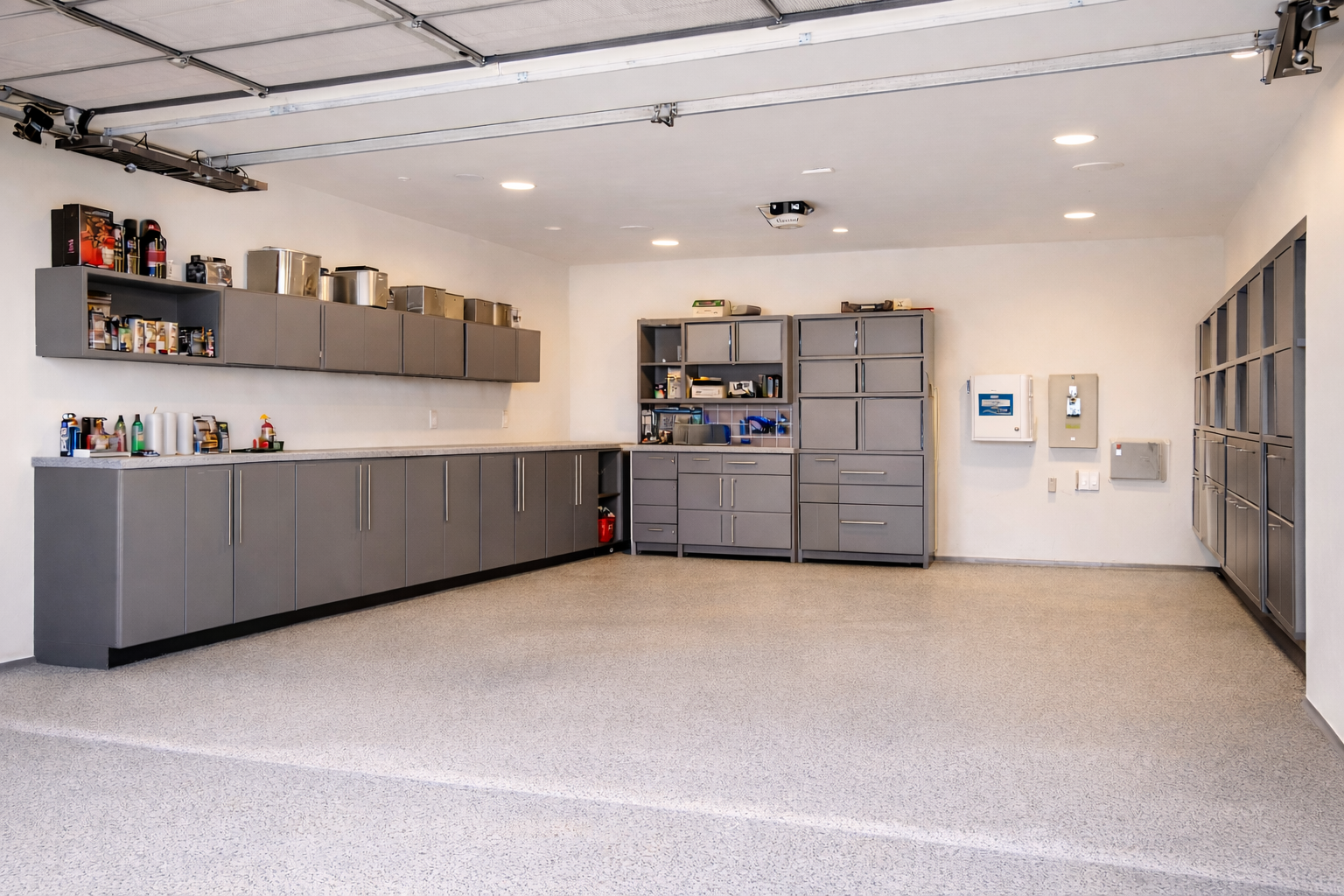 Empty garage with gray cabinets, shelves, and storage lockers on beige carpeted floor.