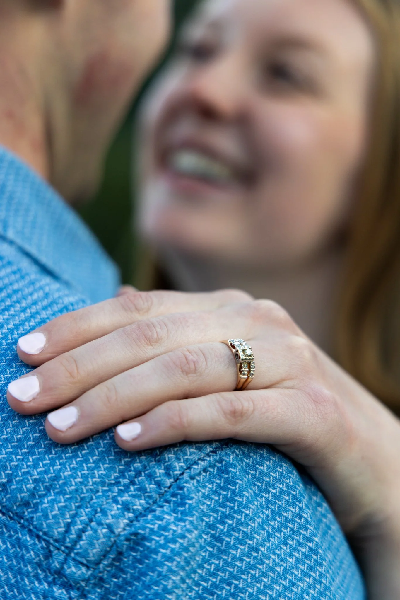 Close-up of a woman's hand with white painted nails, displaying a gold and diamond engagement ring, with focus on the ring.