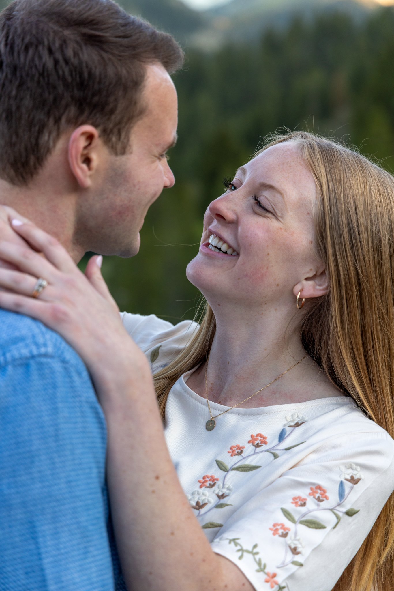 A couple smiling and looking into each other's eyes outdoors, with the woman holding the man's face gently.