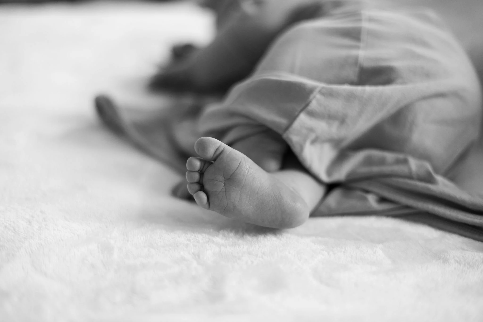 Close-up black and white photo of a small child's hand grasping an adult's finger, lying on a soft surface.