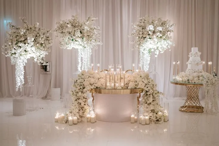 Elegant wedding or special event table setup with white floral arrangements, candles, and soft lighting.
