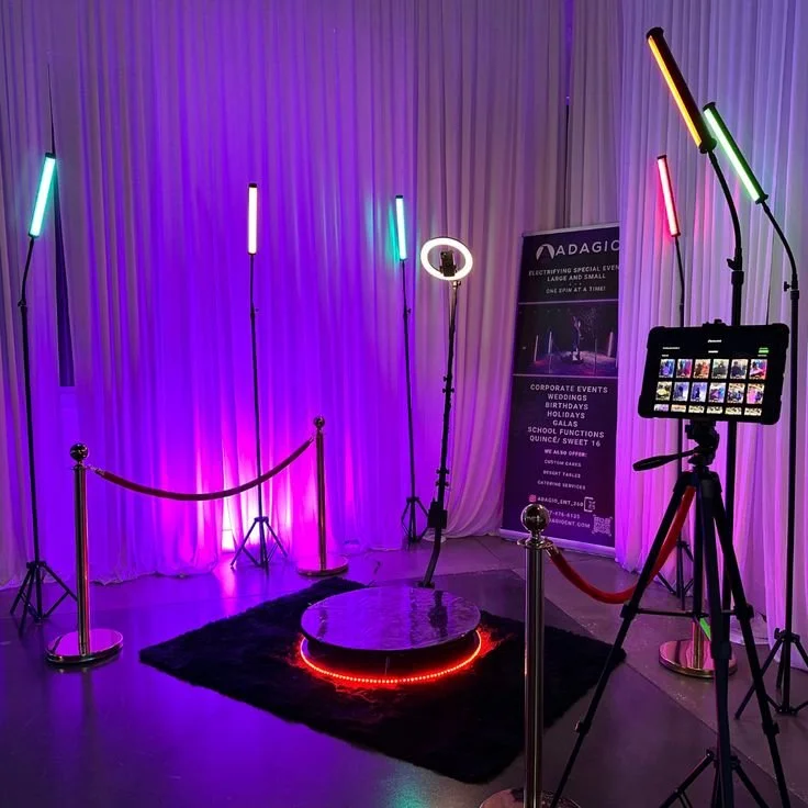 Photography setup with colorful LED light sticks, a ring light, a camera on a tripod, purple curtains, a black rug, and a promotional banner for ADAudio company.