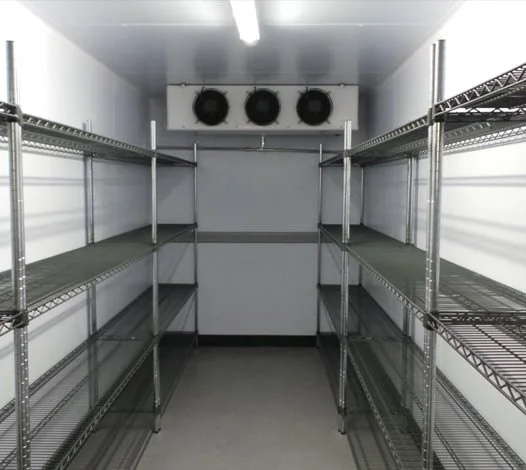 Empty walk-in refrigerator with metal shelving on both sides and three large fans or cooling units on the back wall.