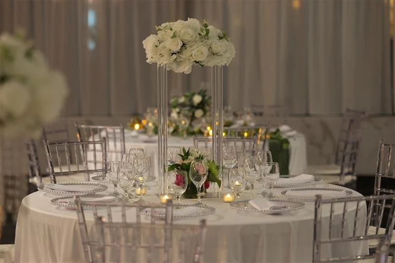 Round banquet table decorated with white floral centerpiece, surrounded by clear chairs, set for a formal event with wine glasses, candles, and elegant place settings.