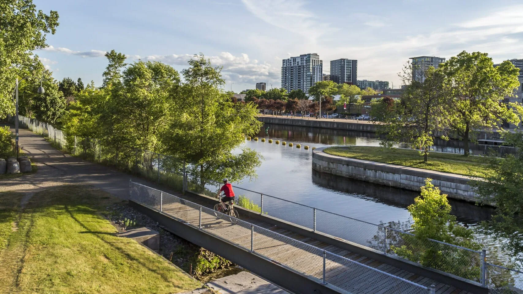 Person riding a bicycle on a bridge over a river in a city park.