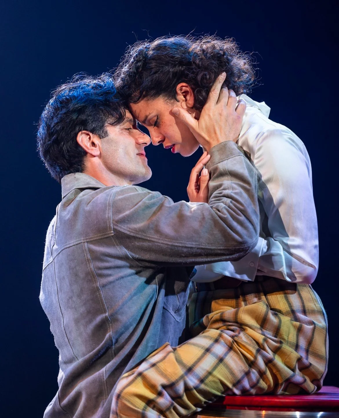 A man and woman are closely engaged, with foreheads touching, holding each other's faces, appearing emotional and intimate.