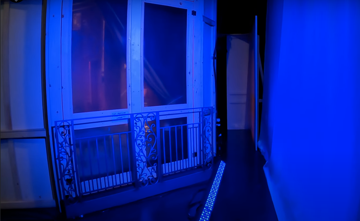 Room illuminated with blue LED lights, with a metal gate and some wooden panels, possibly part of a house or construction site.