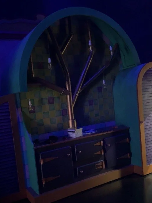 The image shows a decorative wall with a large tree design, integrated with branches and hanging light bulbs, and a black countertop below it.