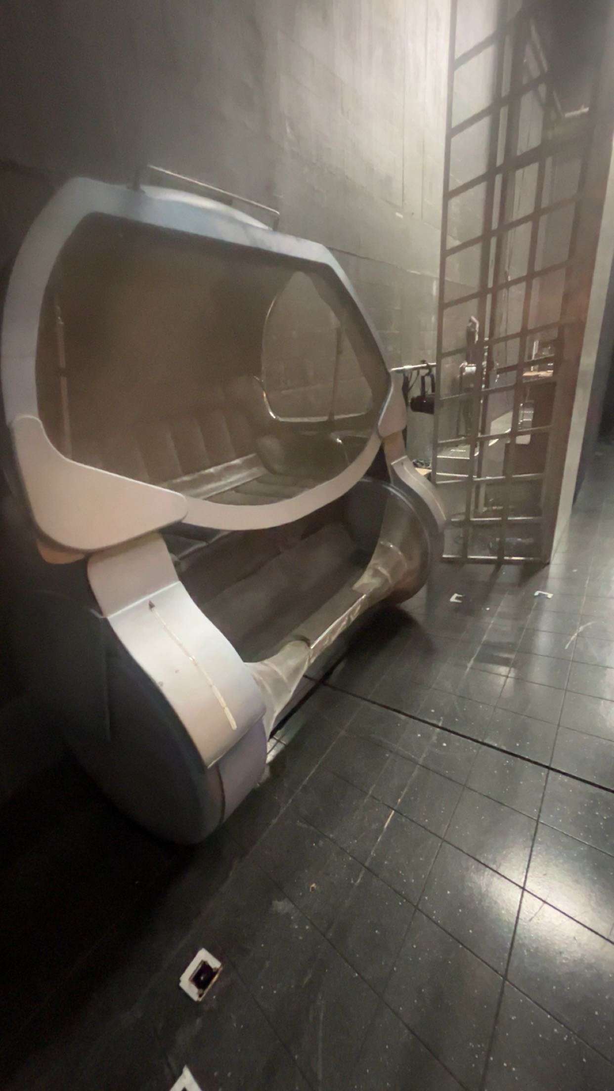 An empty photon shower with black tiled flooring, a gray wall, and a metal security gate next to it.